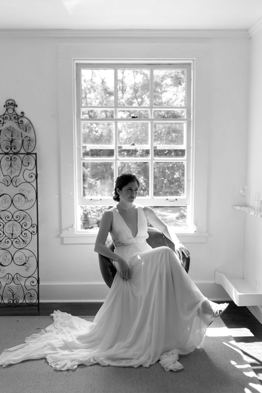 A series of black and white photos showing a figure in a flowing white wedding dress posing by sunlit windows.
