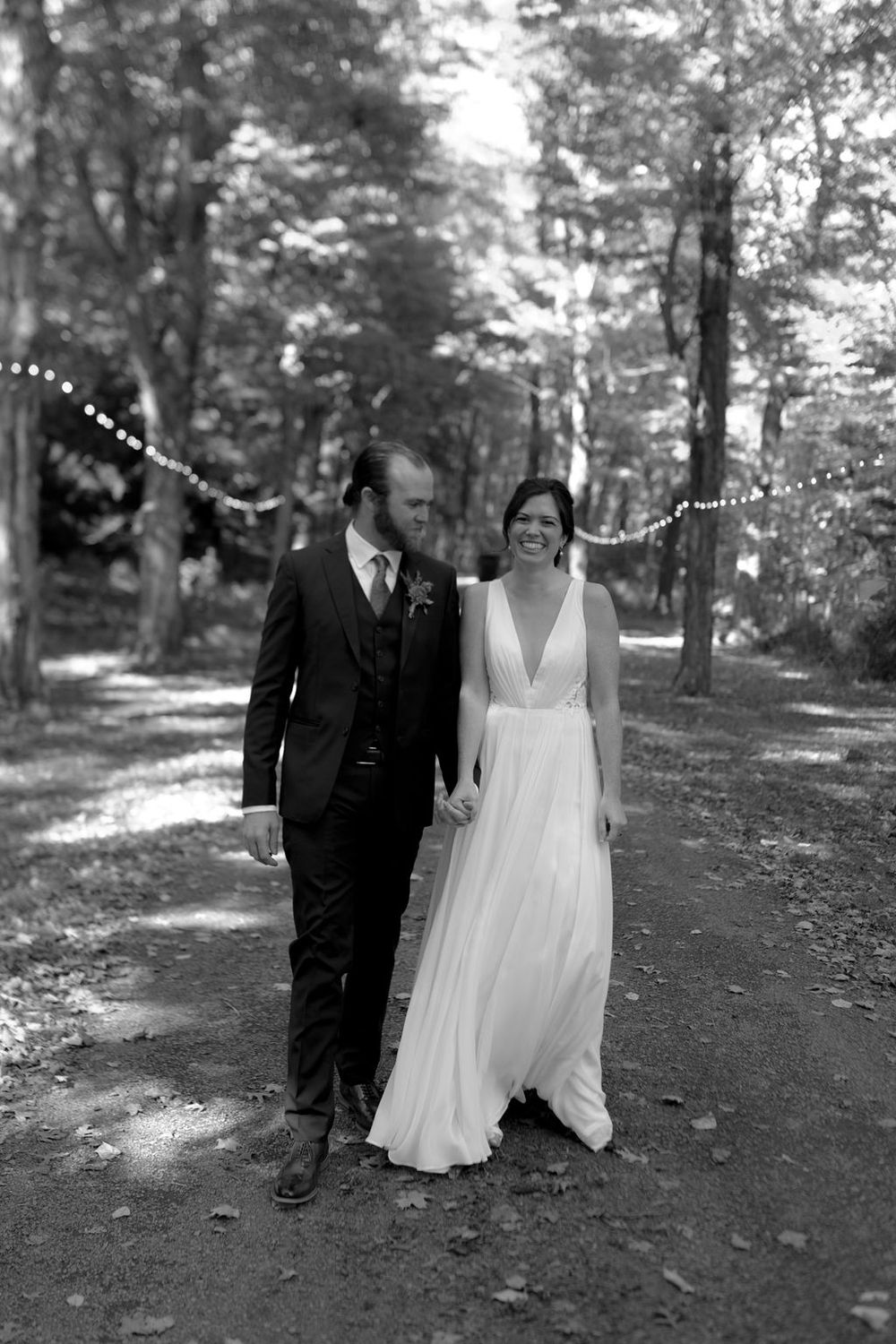 Black and white wedding photos of a couple walking and posing together on a tree-lined outdoor path.