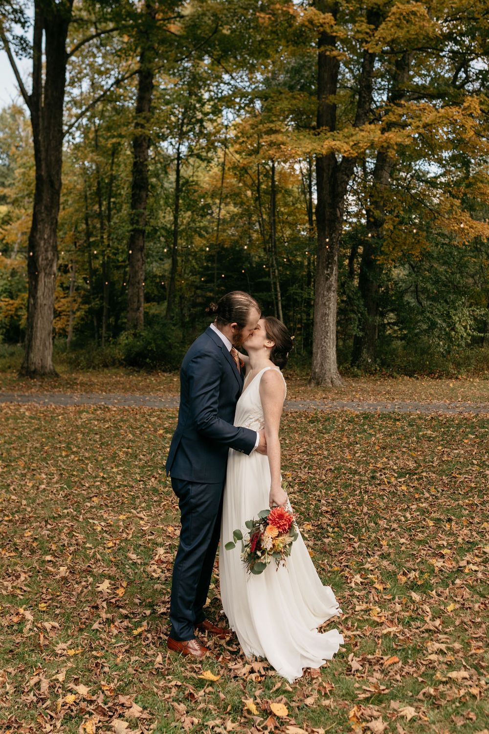 Romantic autumn wedding portrait in a forest with golden leaves scattered on the ground.