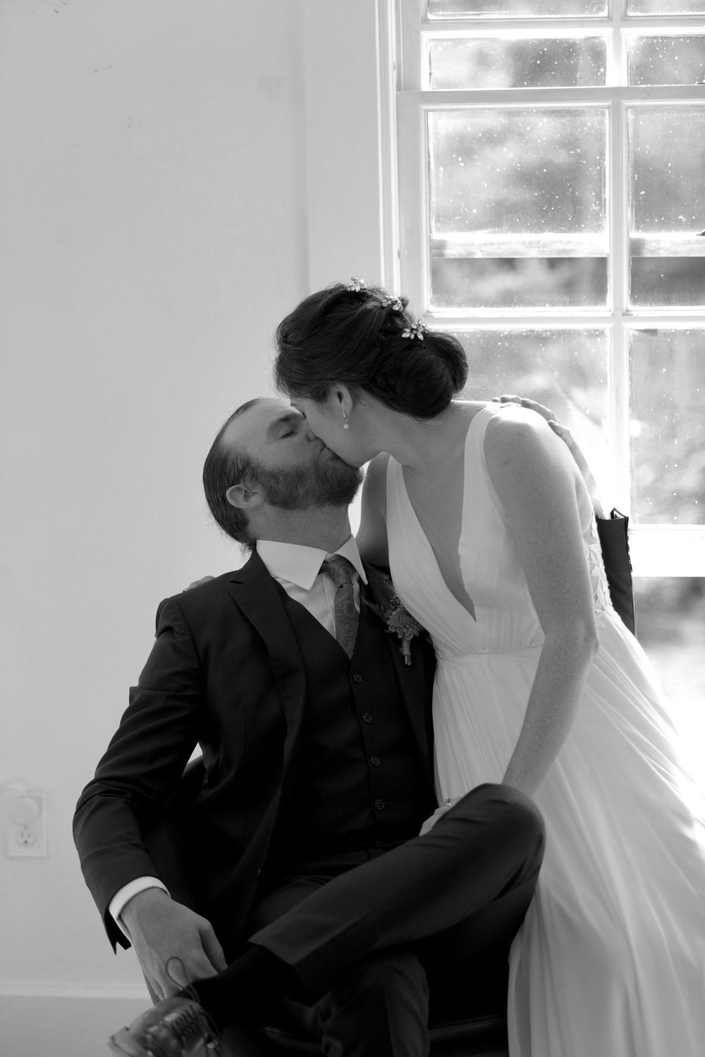 A tender moment between newlyweds in front of bright windows in a white room.