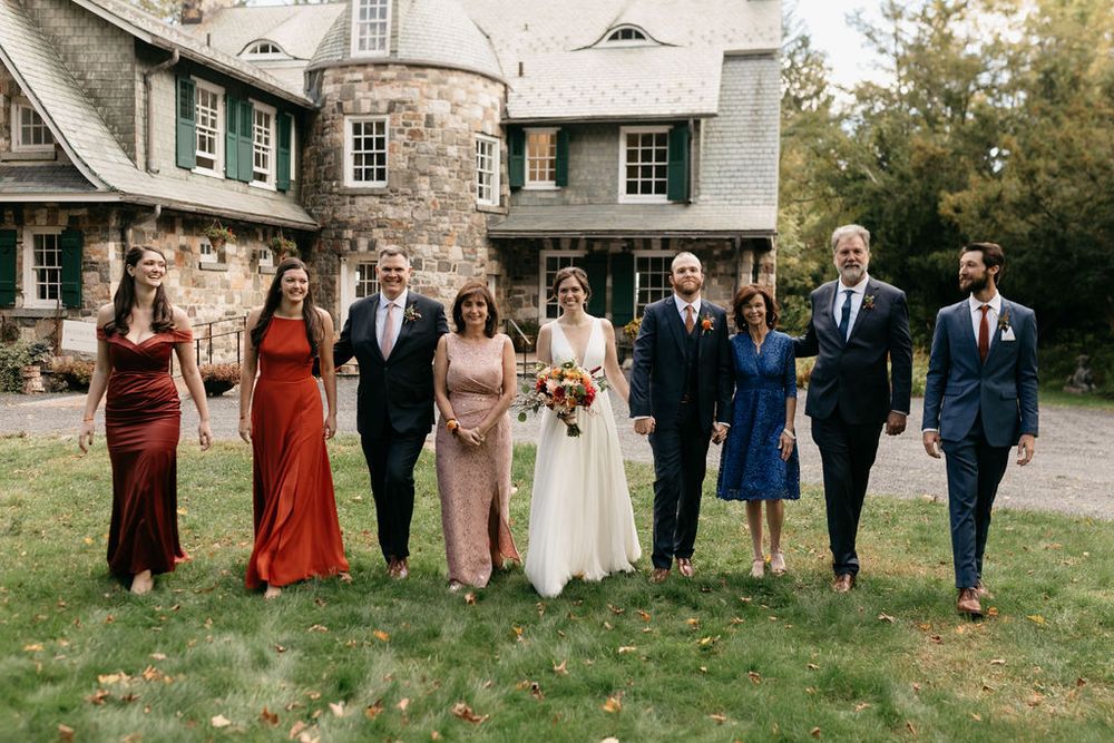 Wedding party members walk together on a stone path wearing coordinated formal attire in burgundy and navy blue colors.