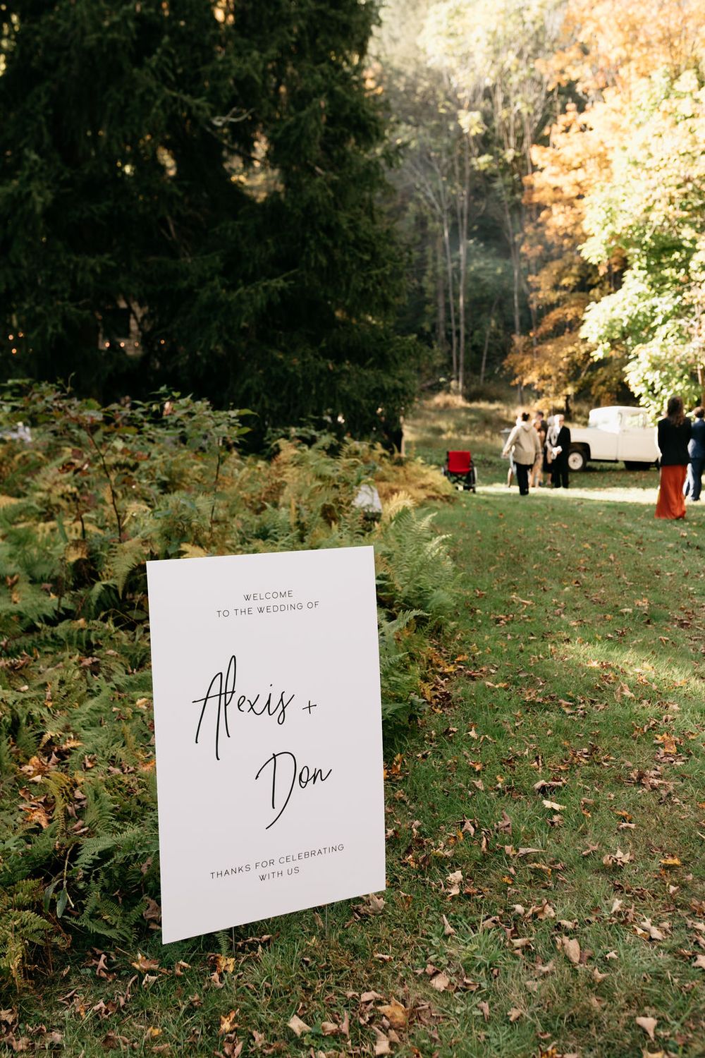 White wedding signage displayed on a grassy lawn with autumn trees and foliage in the background.