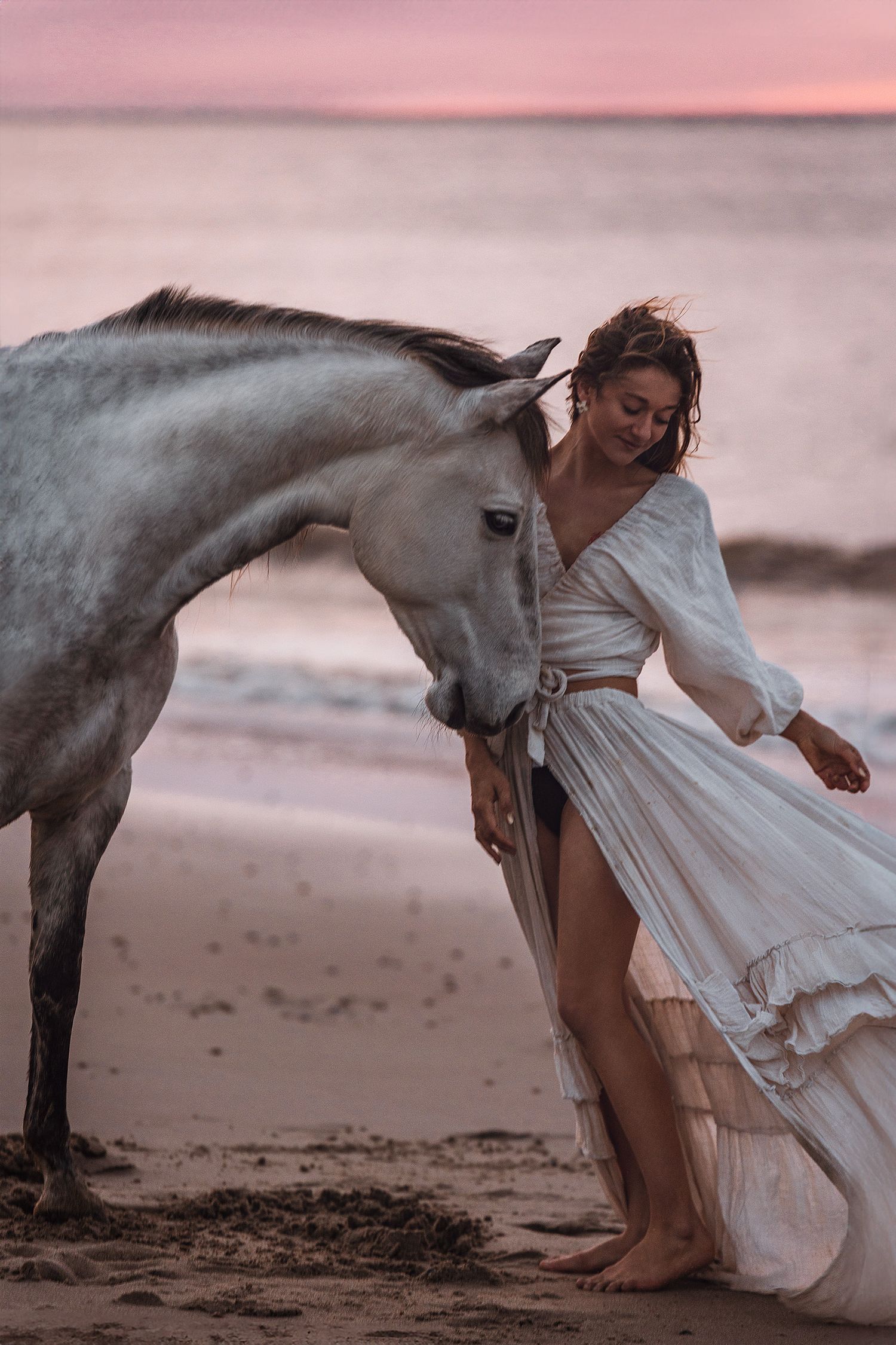 Junge Frau mit langem Kleid und weißem Pferd wird am Strand von Madlen Becker Photography fotografiert