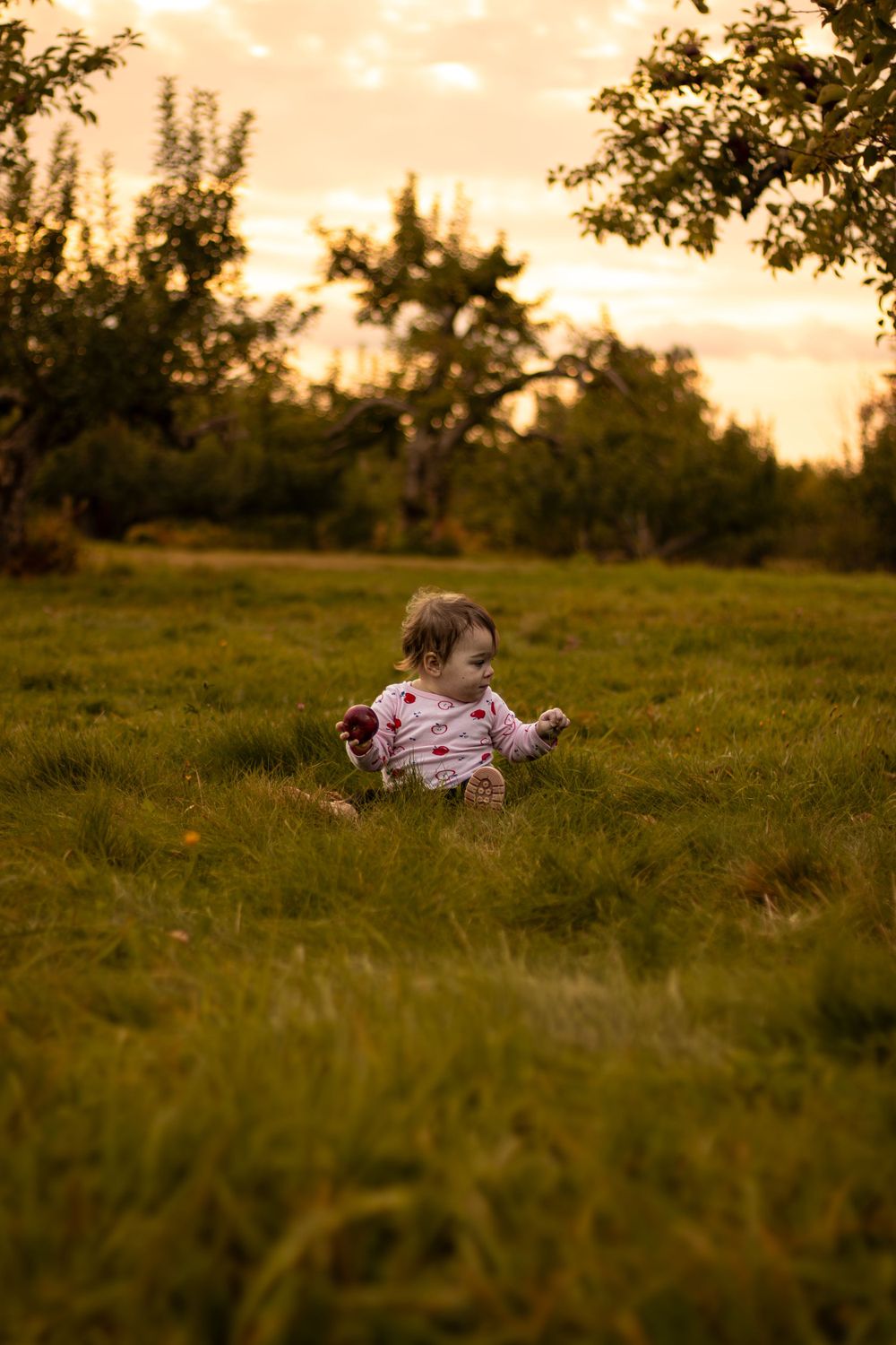 A small child in a pink patterned outfit lying on grass during golden hour sunset.
