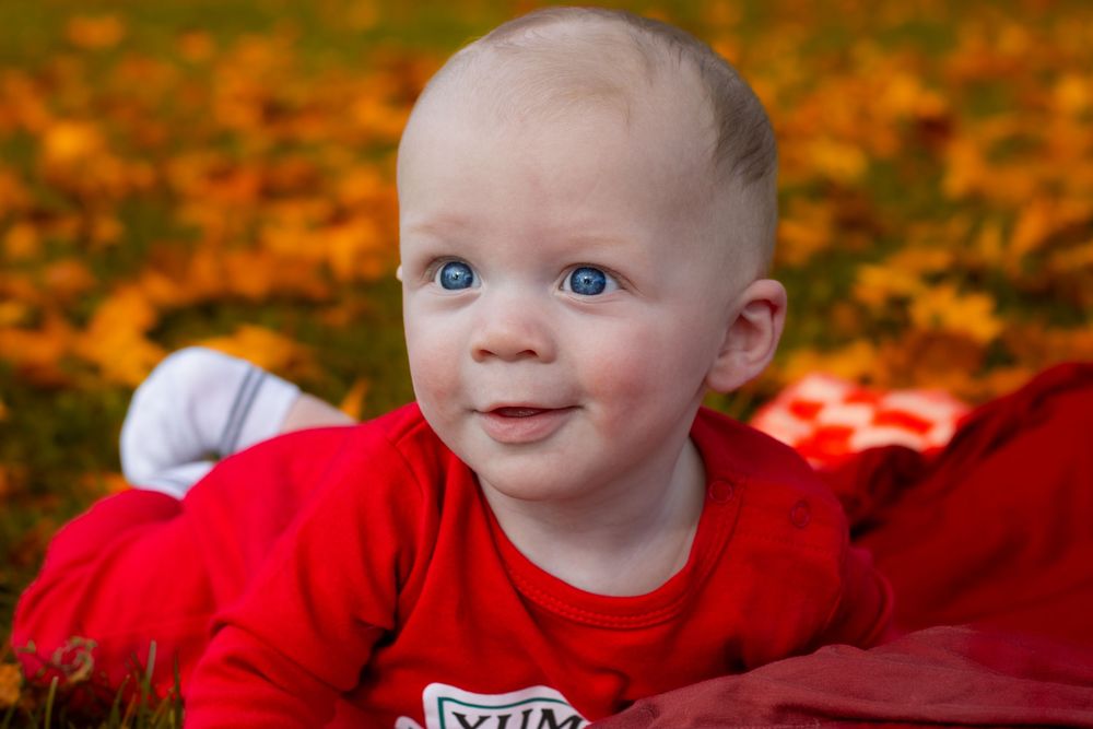 A small child in red clothing smiles while lying on autumn leaves.