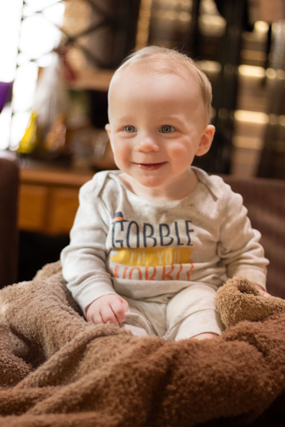A smiling baby in a white onesie with text lies on a cozy brown blanket in a series of three photos.