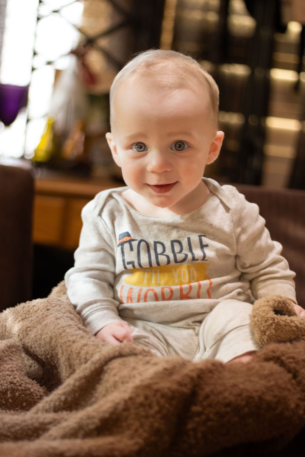 Baby wearing a white 'Gobble' shirt smiles while lying on a brown blanket.