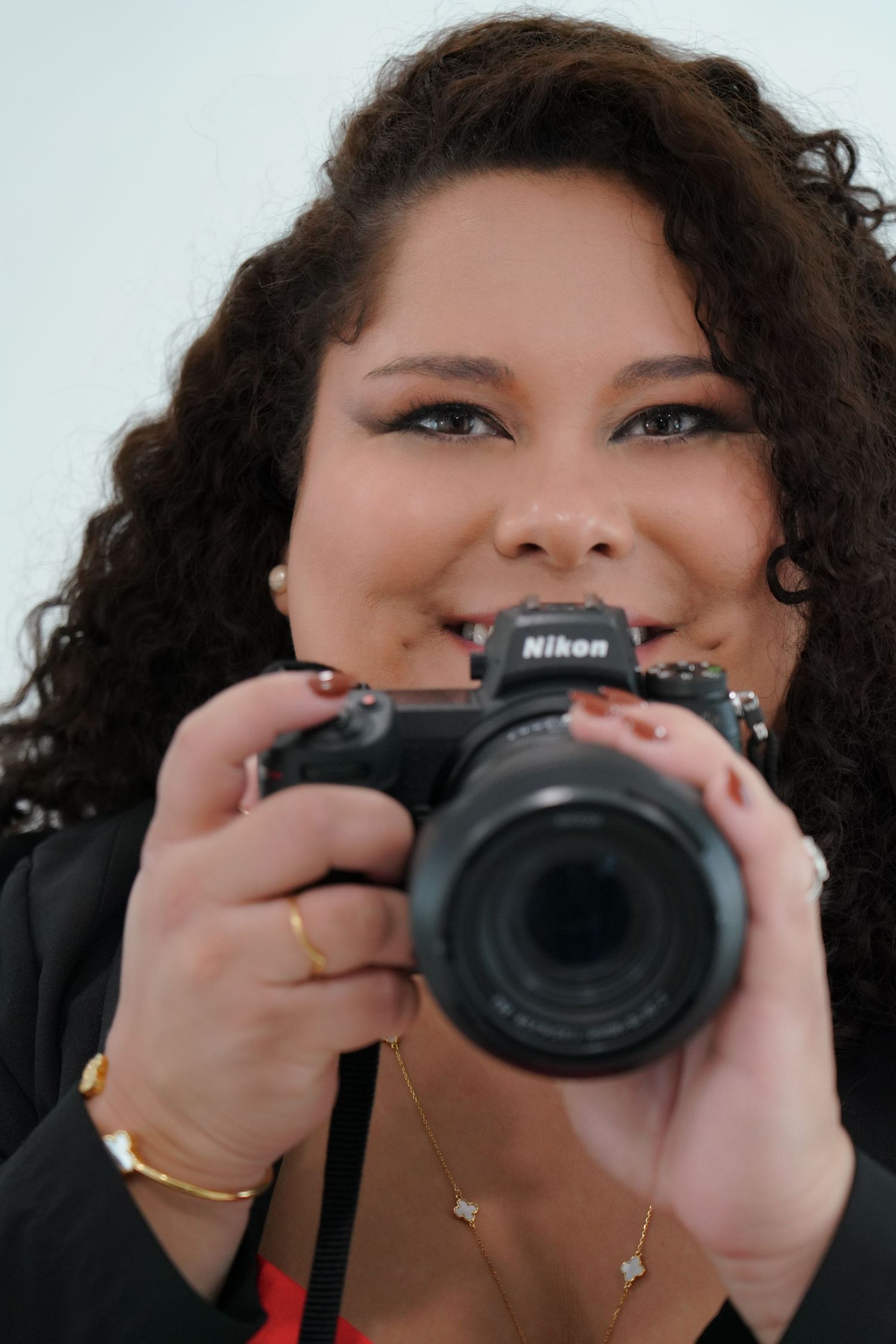 Photographer smiles while holding Nikon camera in professional headshot.
