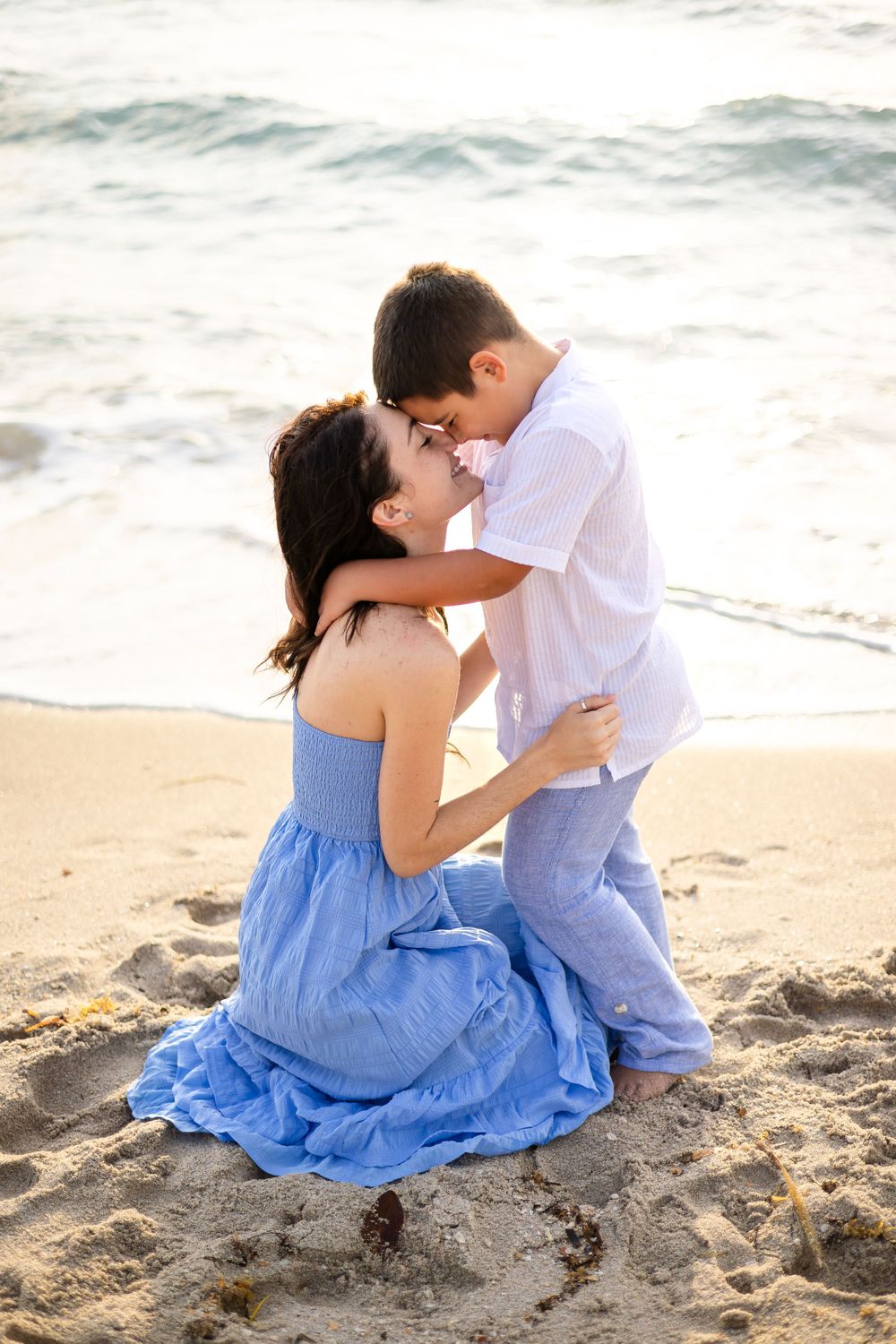 An intimate moment captured between two people embracing on a sandy beach with waves in the background.