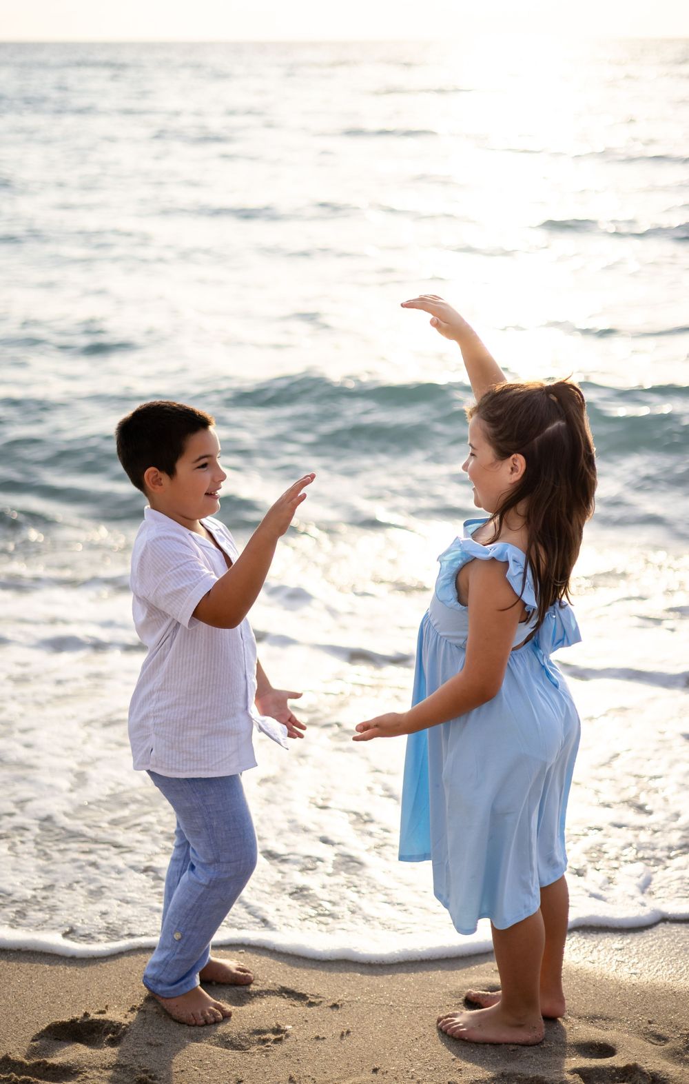 Two people in coordinating outfits playfully interact on a beach at sunset.