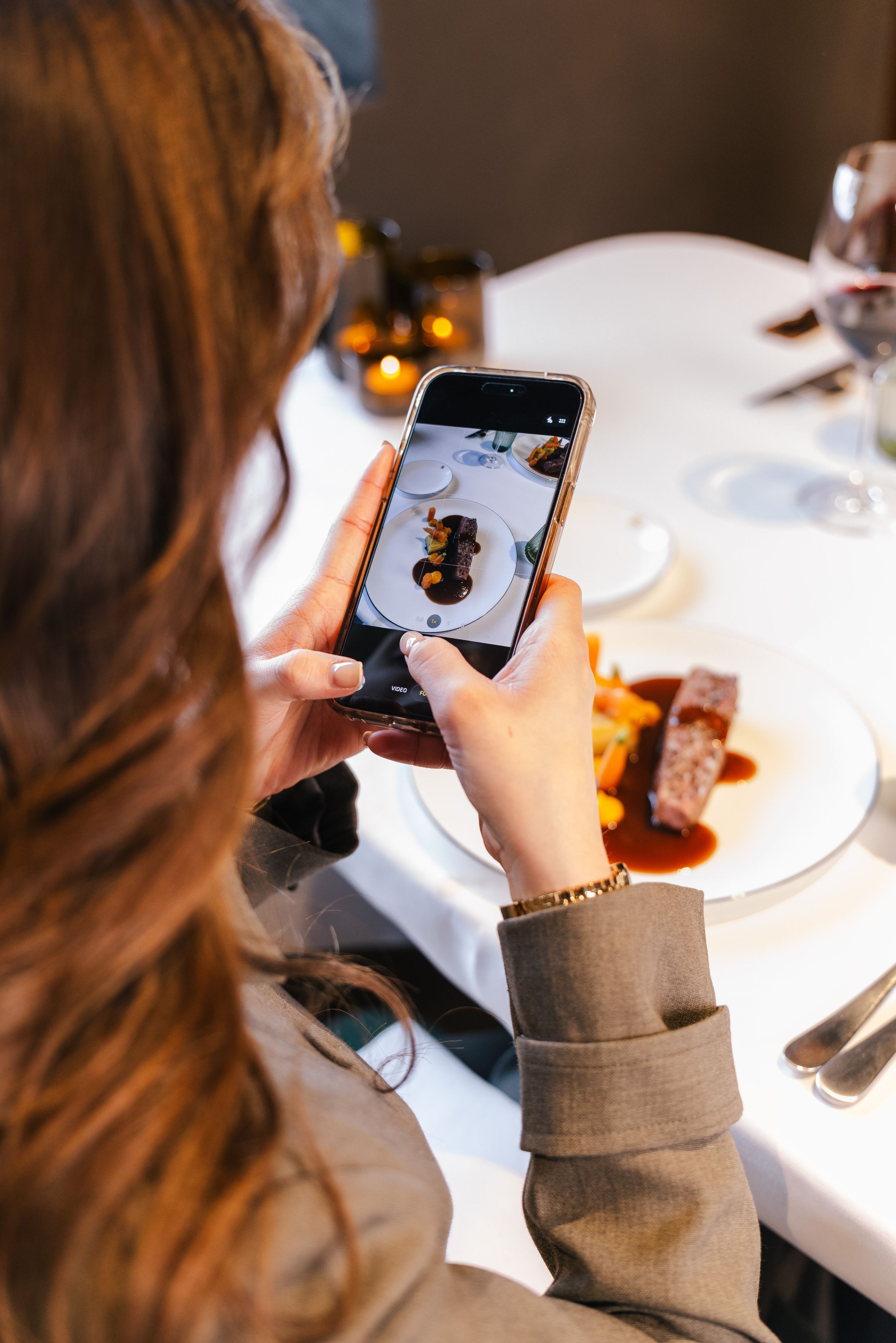 Woman photographing a gourmet meat dish with red wine sauce on her smartphone at an elegant restaurant.