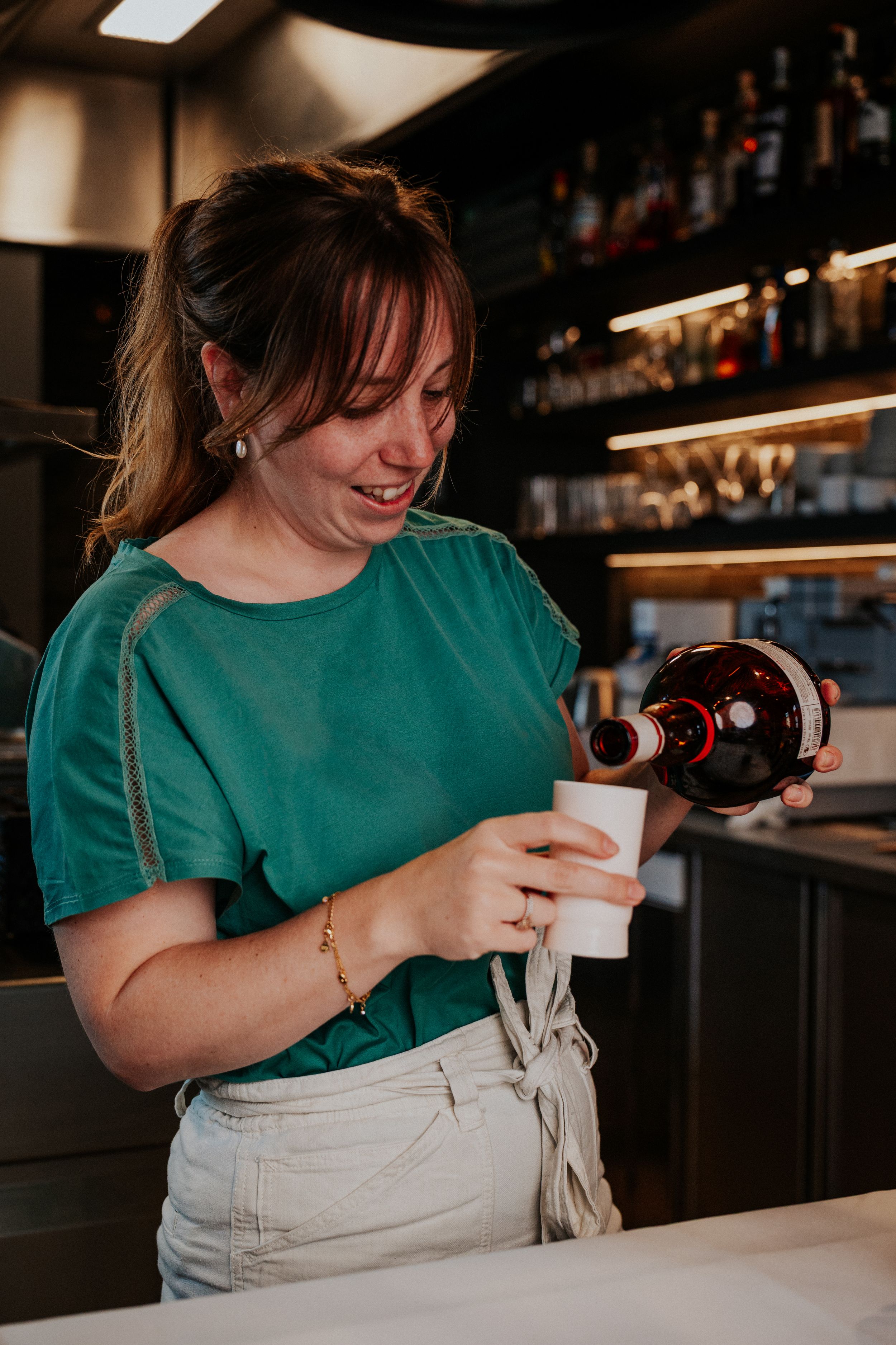 Person in green shirt pouring wine at restaurant bar counter.