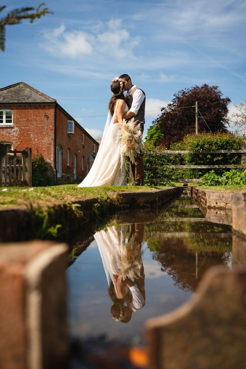 Bride & Groom kissing with reflection in water at Cadhay House