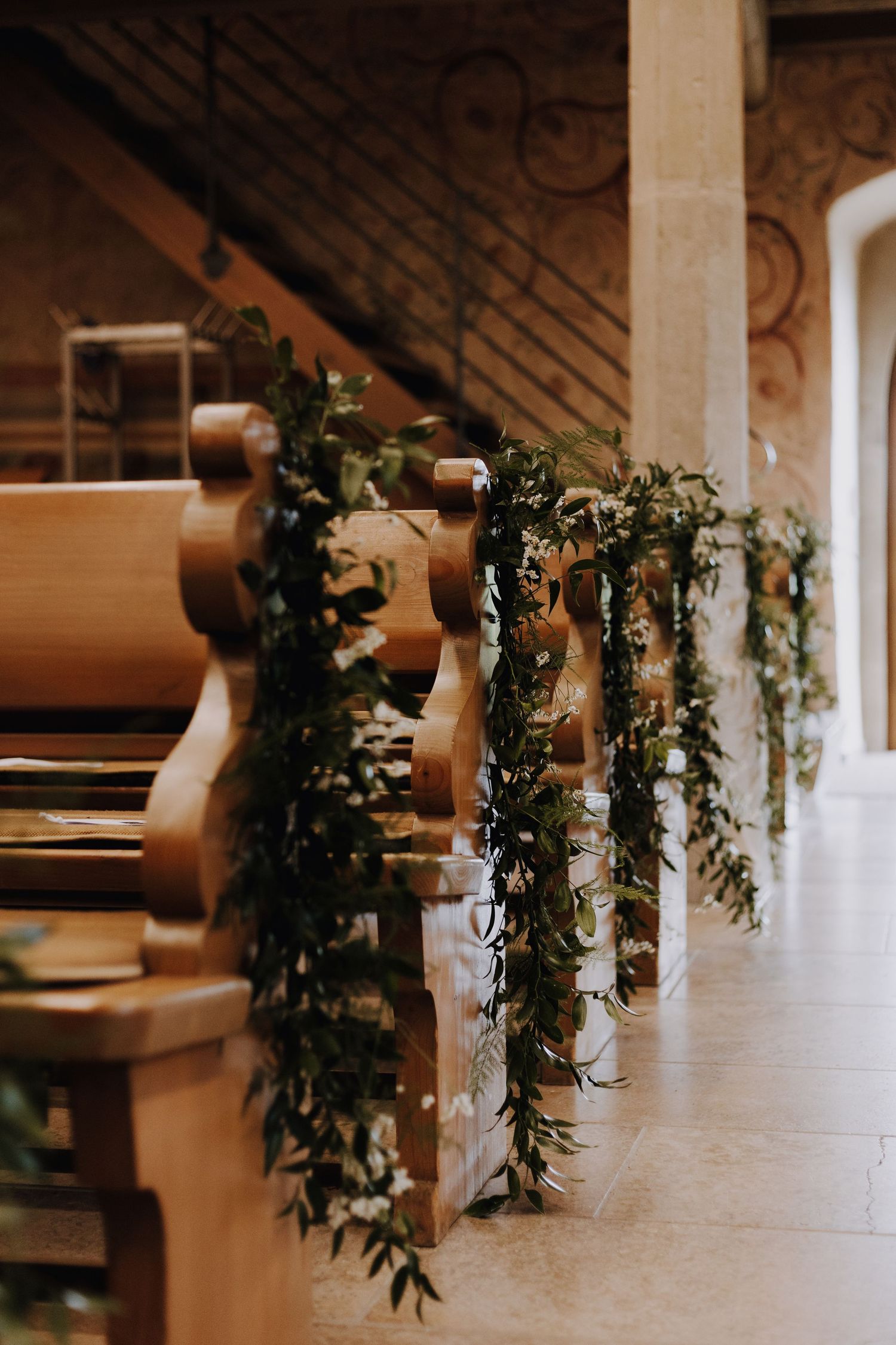 Church pews decorated with cascading greenery garlands create a romantic wedding ceremony setting.