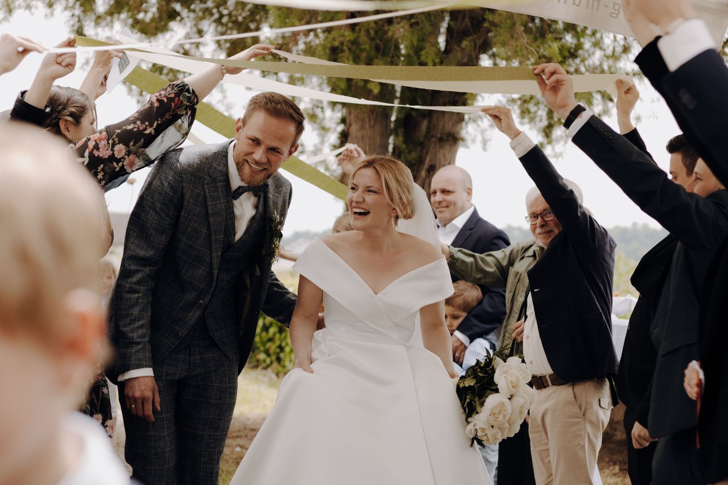 Wedding guests form an arch with their arms as newlyweds walk beneath during outdoor ceremony reception.