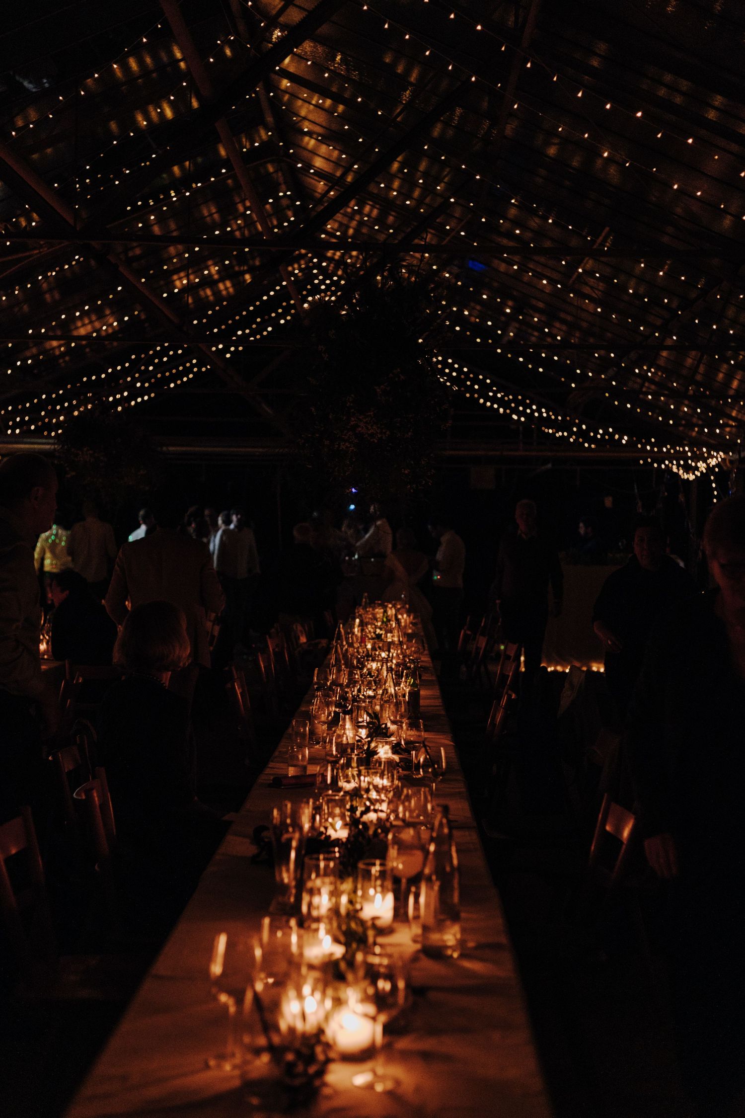 Romantic candlelit table setting with string lights creating atmosphere at evening wedding reception.