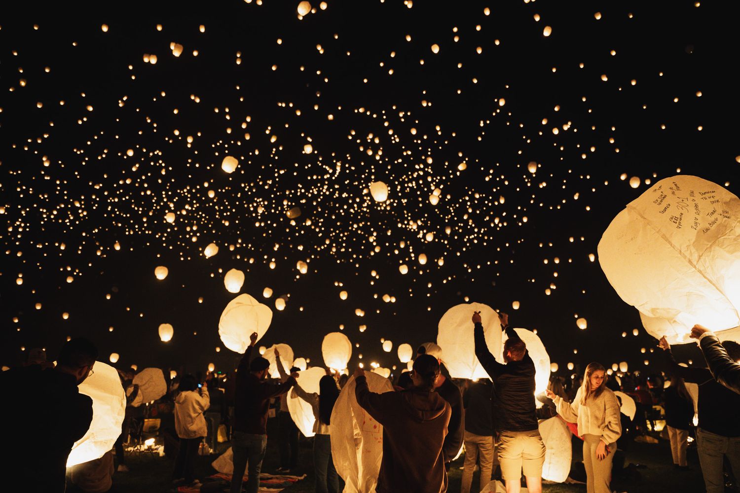 A crowd releases glowing paper lanterns into the night sky creating a magical display of floating lights.
