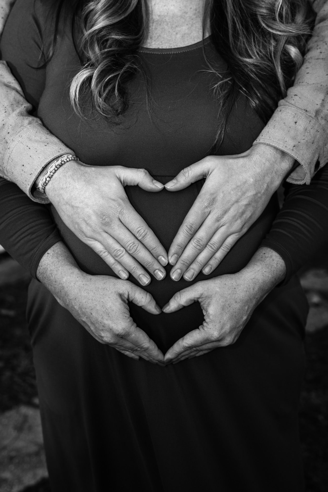 Hands forming a heart shape over a pregnant belly in black and white.