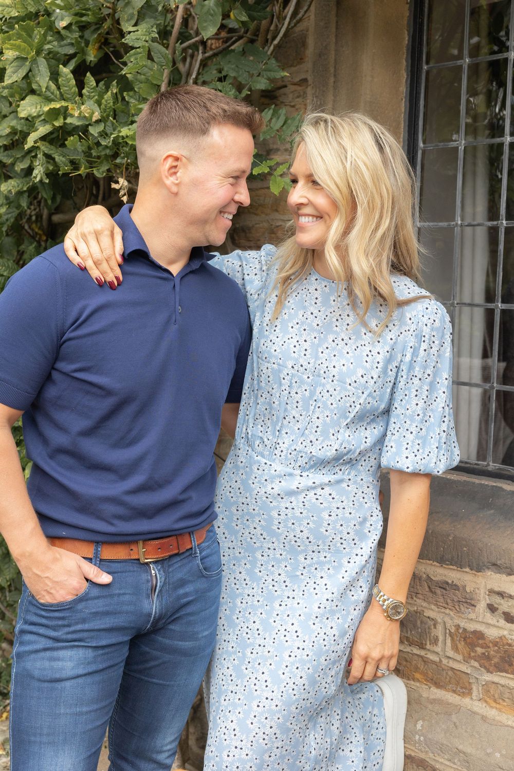 A couple in blue outfits share affectionate moments in a series of romantic outdoor photos against a stone wall.