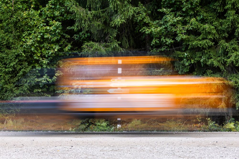 Motion blur of orange rally car speeding through forest track.