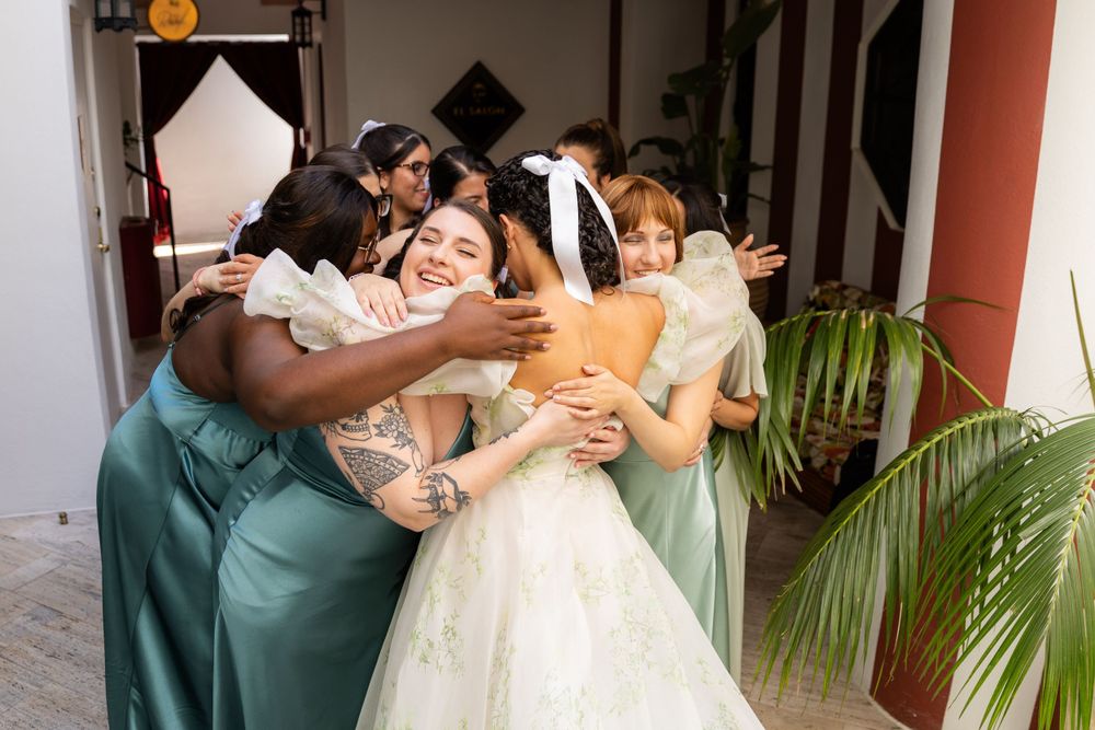Wedding party group hugging and celebrating in a covered outdoor walkway.