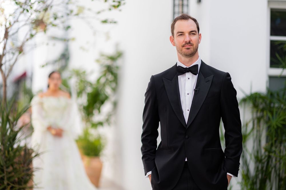 A classic black and white wedding portrait showcasing formal attire against a light-colored wall.