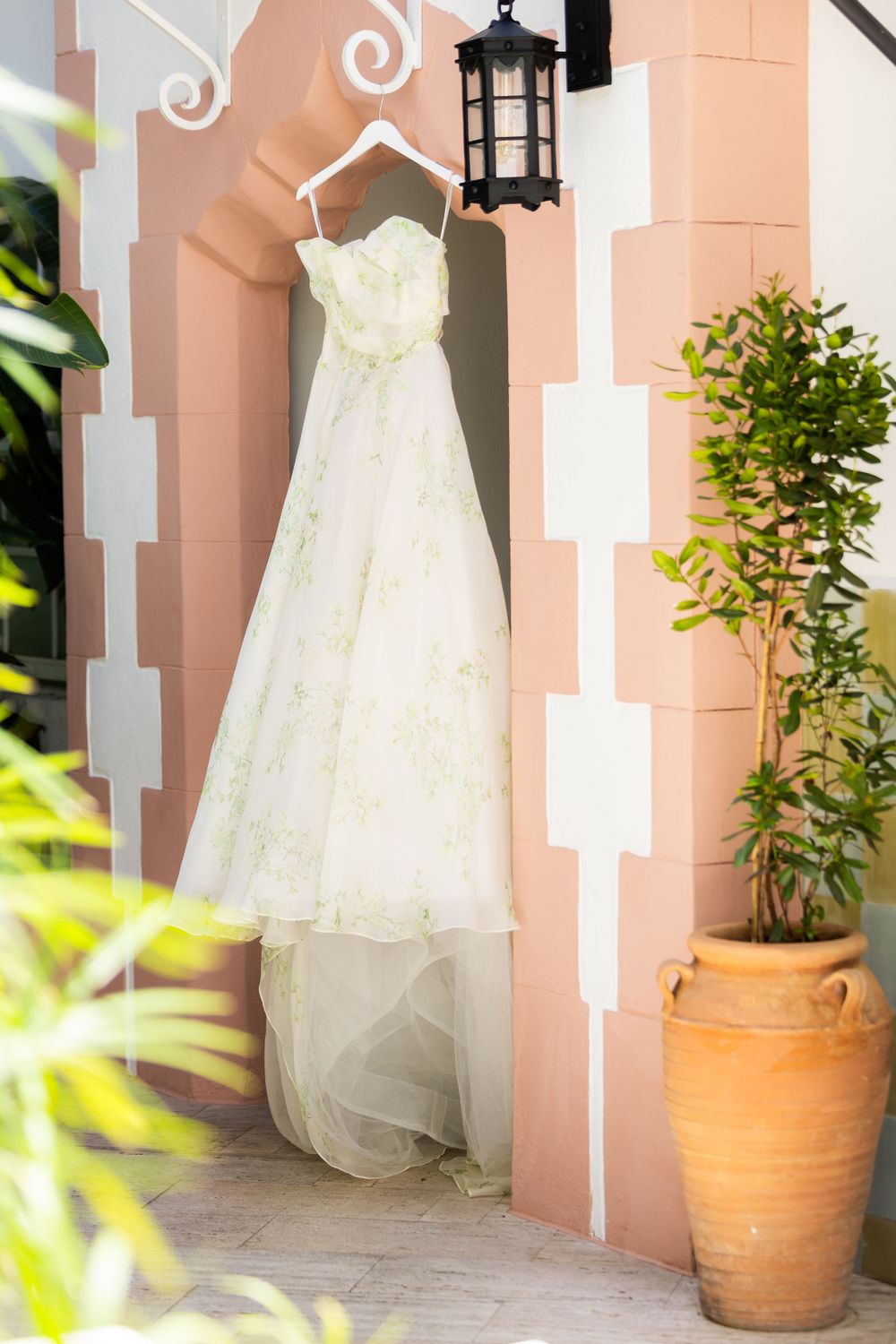 White wedding dress hanging against a coral-colored wall with decorative architectural details.