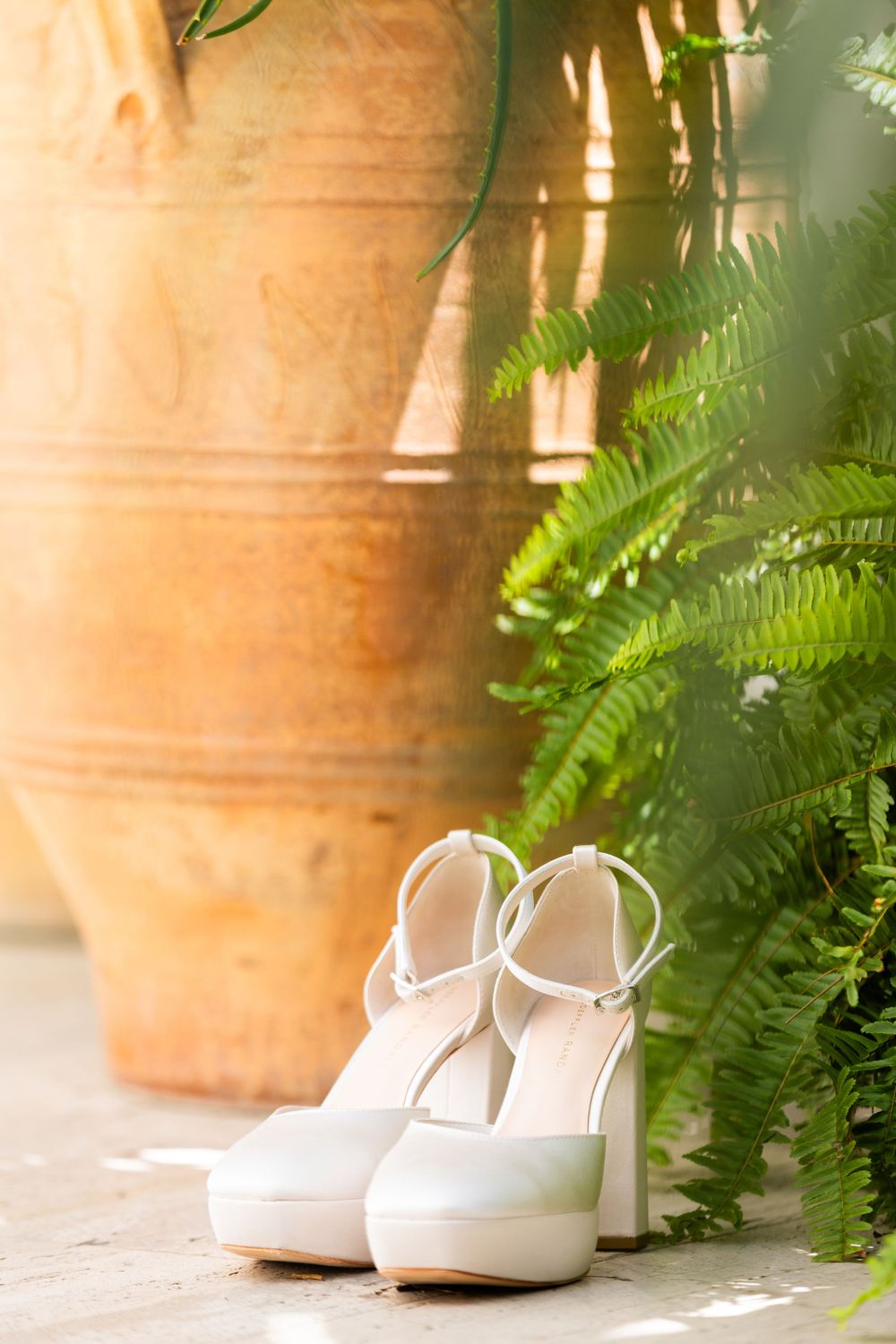 White bridal shoes displayed alongside ferns and terracotta planters in natural lighting.