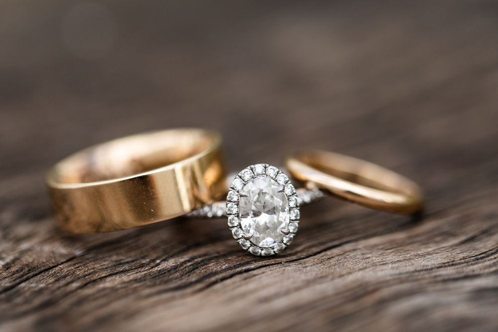 Diamond engagement ring and wedding bands arranged on rustic wooden surface.