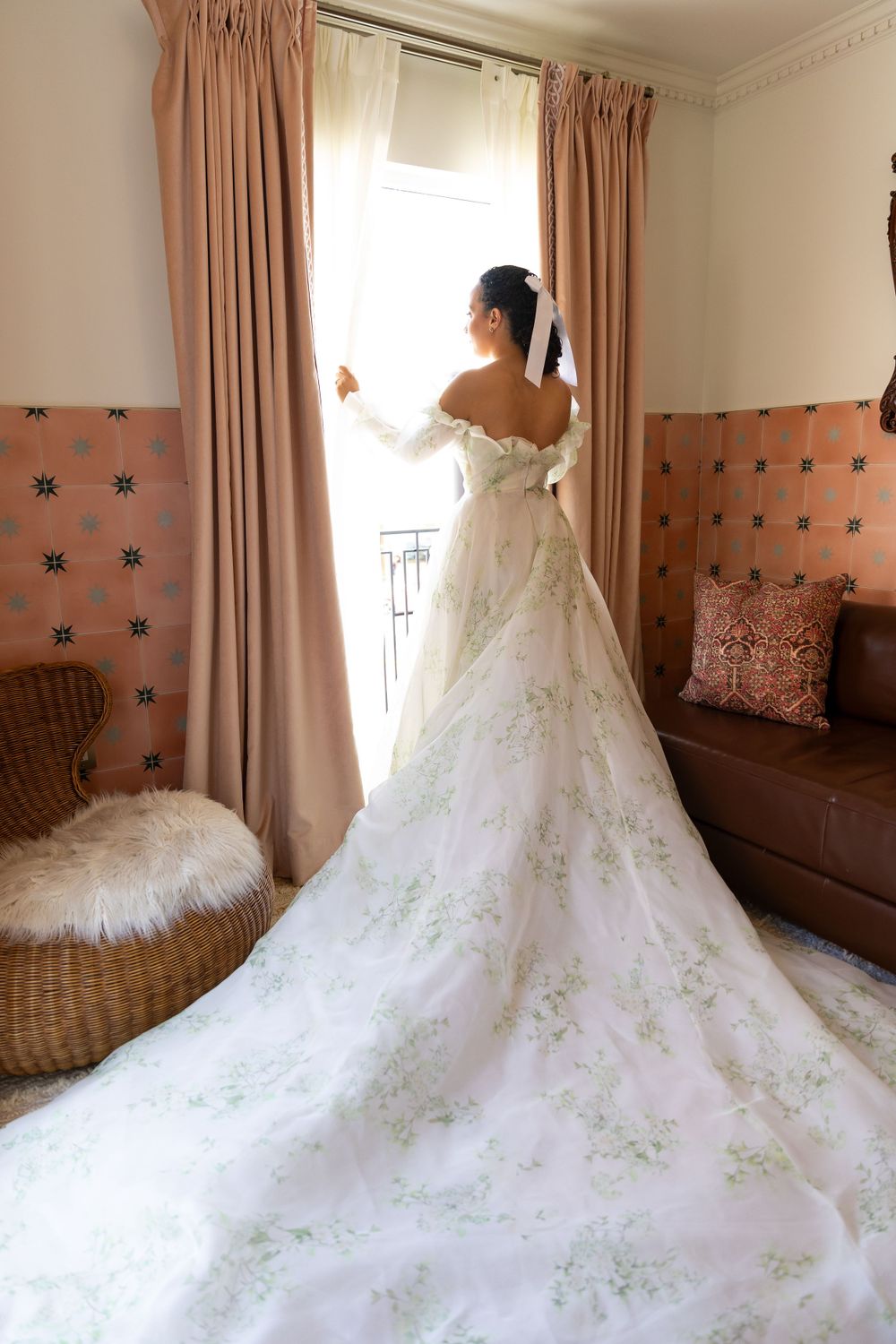 Flowing white wedding gown with intricate details spread across a room with pink curtains.