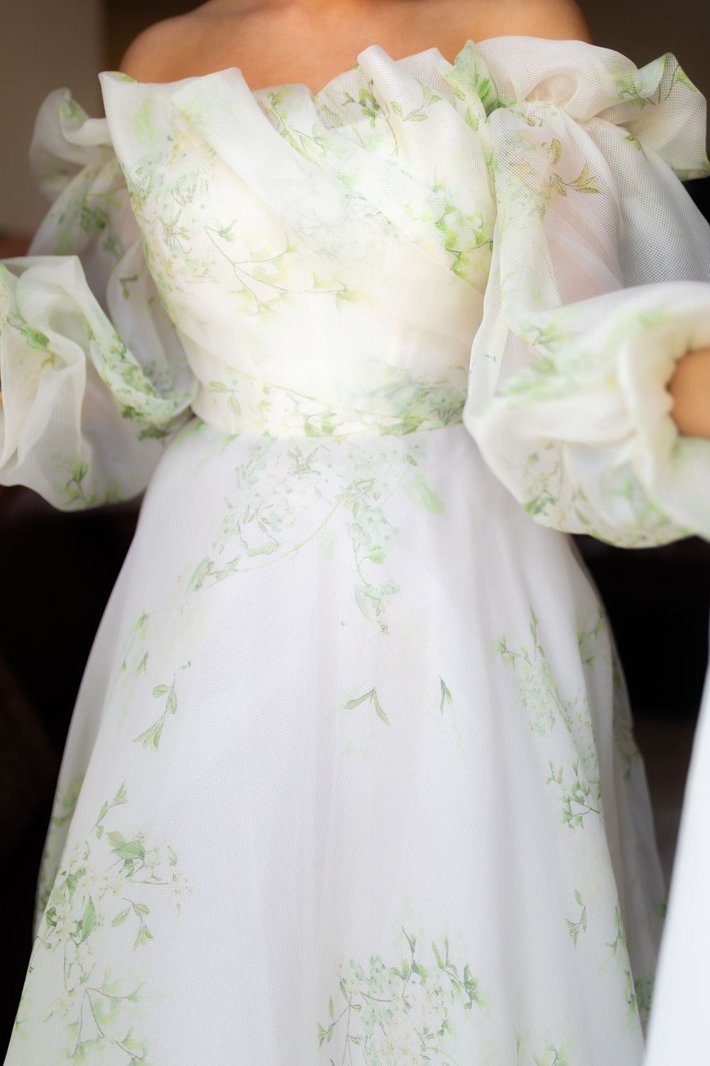 Close-up of wedding dress bodice showing delicate white fabric with light green embroidered details.