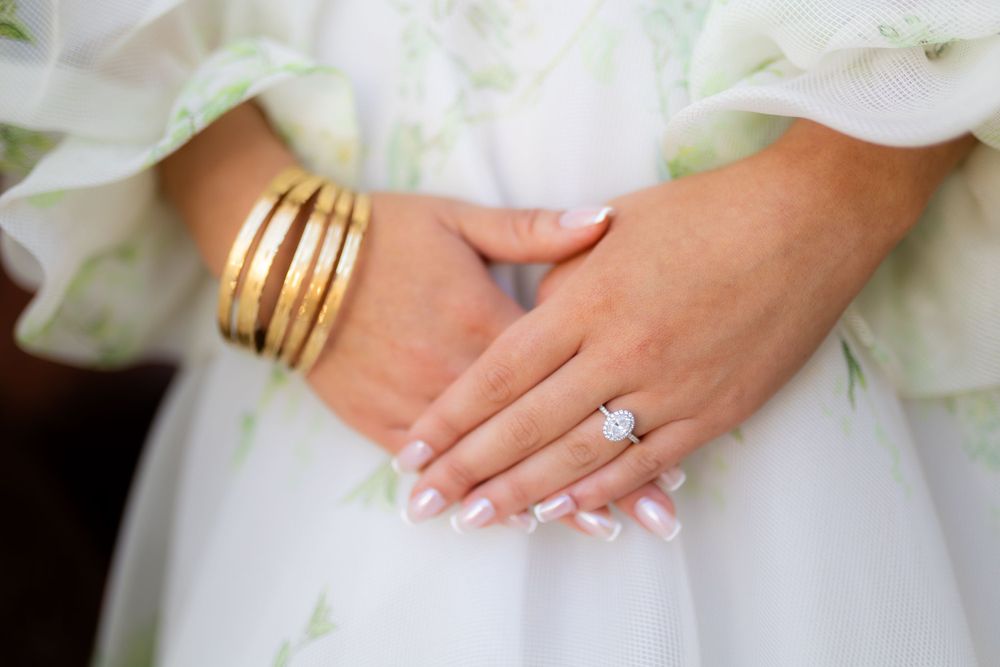 Close-up details of a bride's wedding day accessories including gold rings and white dress fabric.
