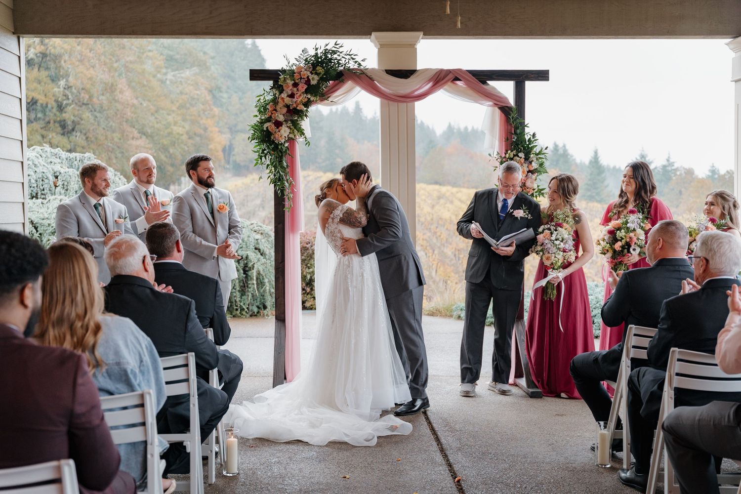 Beautiful outdoor wedding ceremony under rustic wooden arch decorated with flowers and greenery at mountain venue.