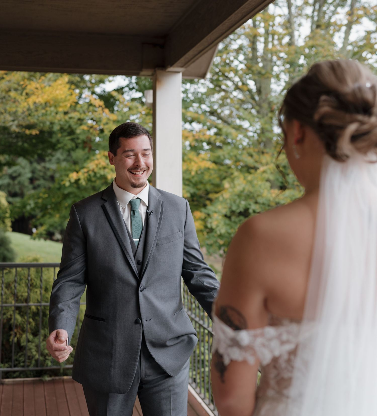 A wedding first look moment captured on a covered porch with fall foliage in the background during their special day.
