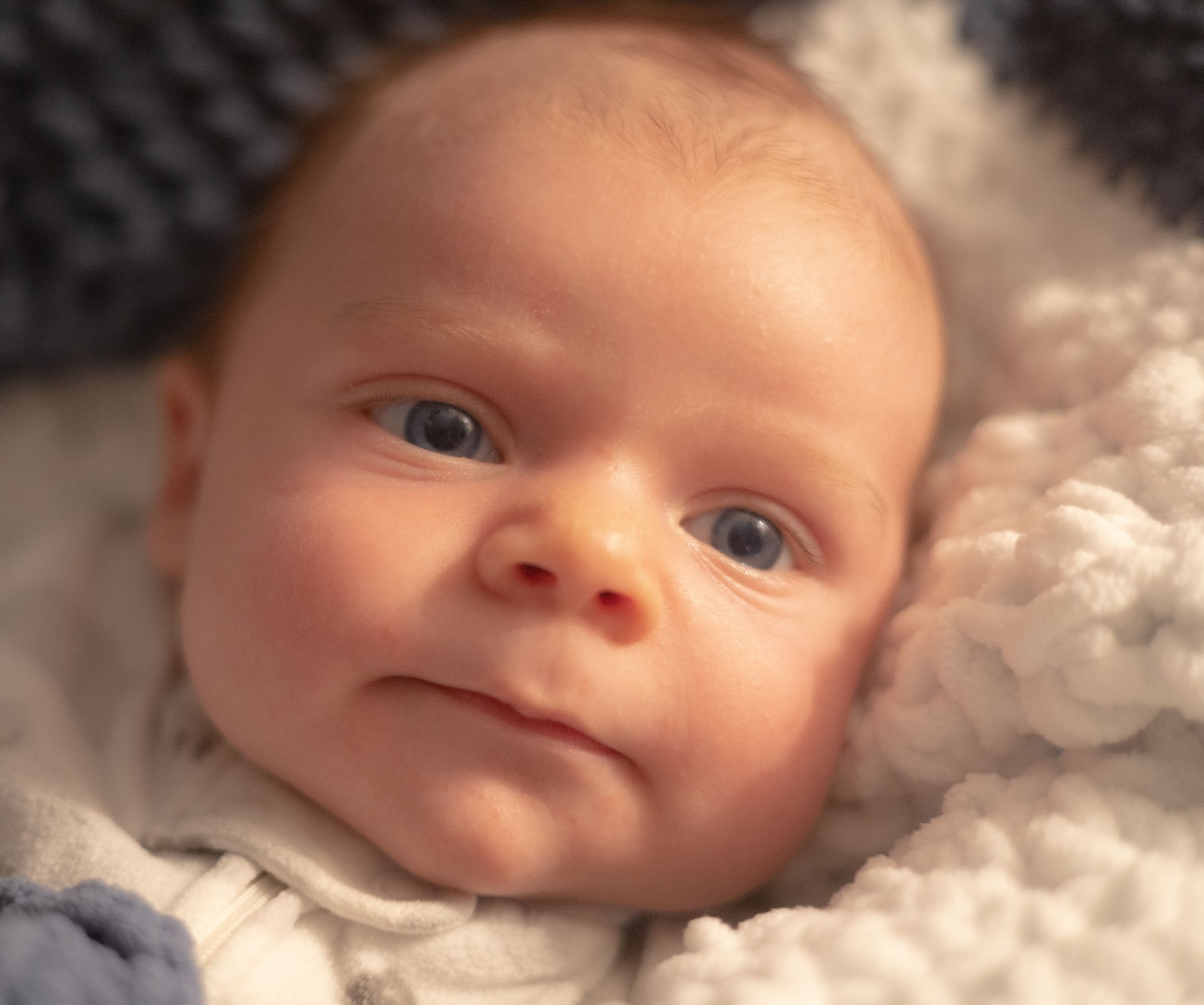 Close-up portrait of an infant lying on soft white blankets.
