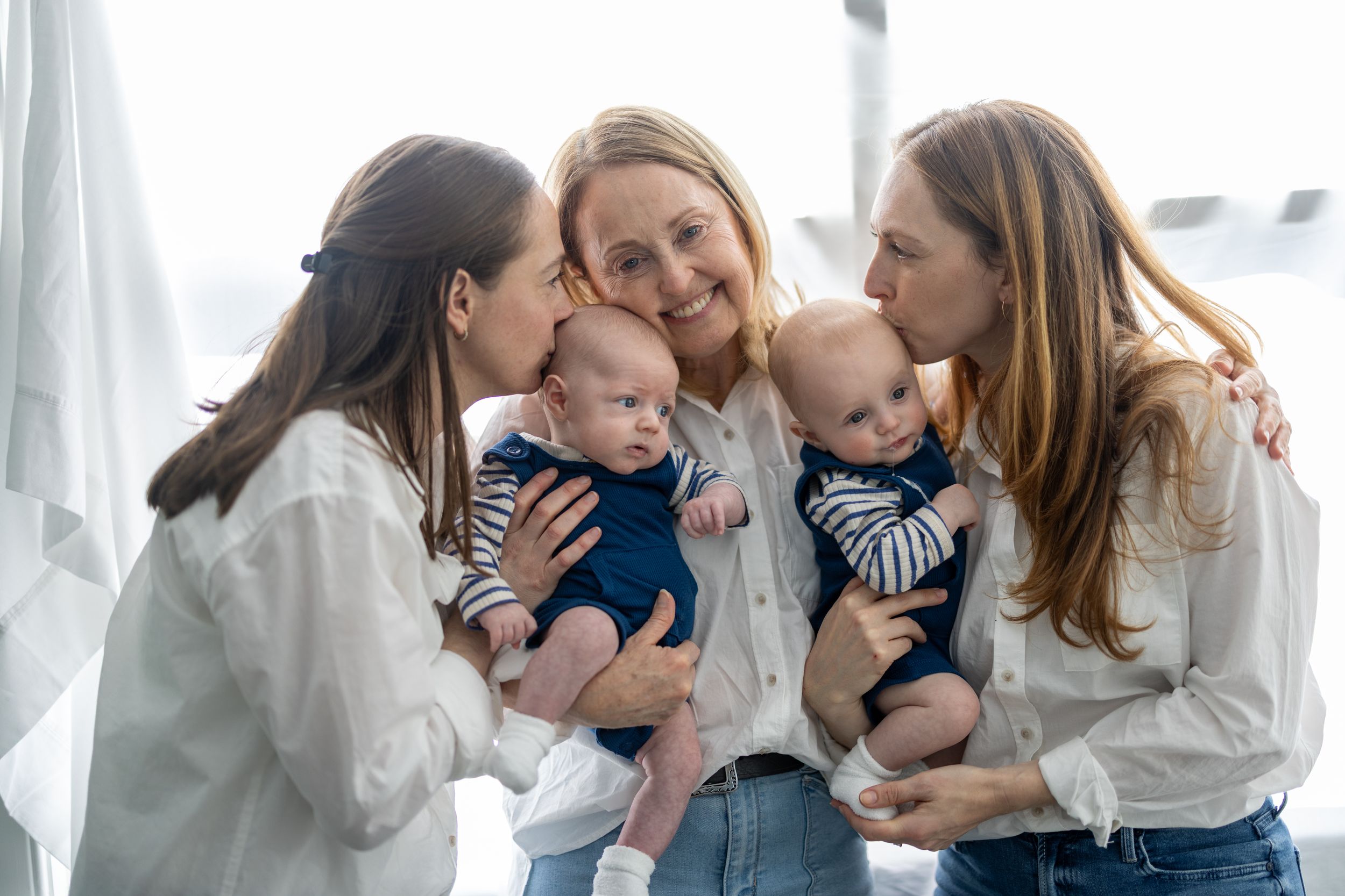 Three people in white blouses share a joyful moment while holding two babies wearing matching striped outfits.