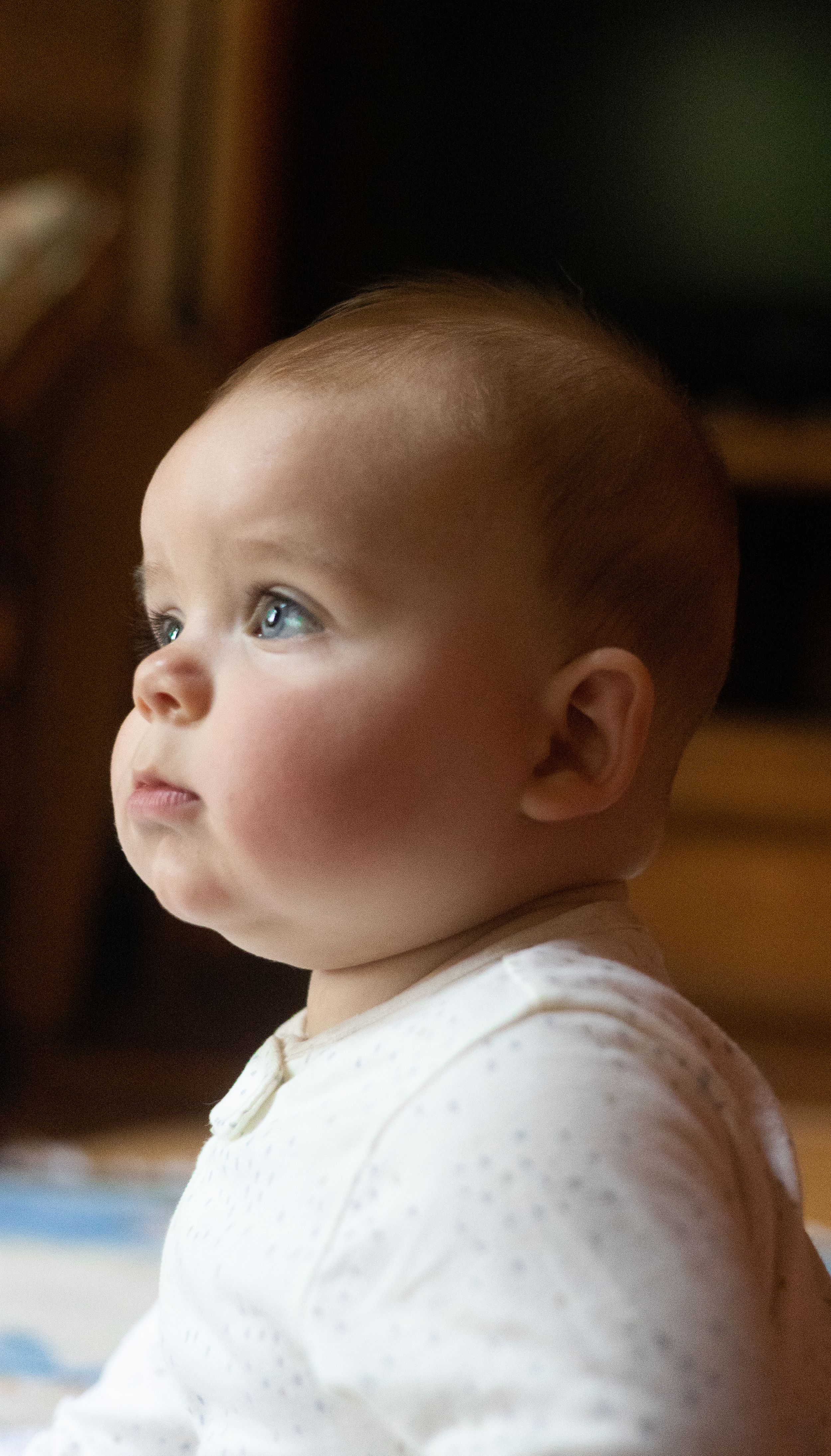 Baby in white outfit gazes upward with wonder and curiosity.