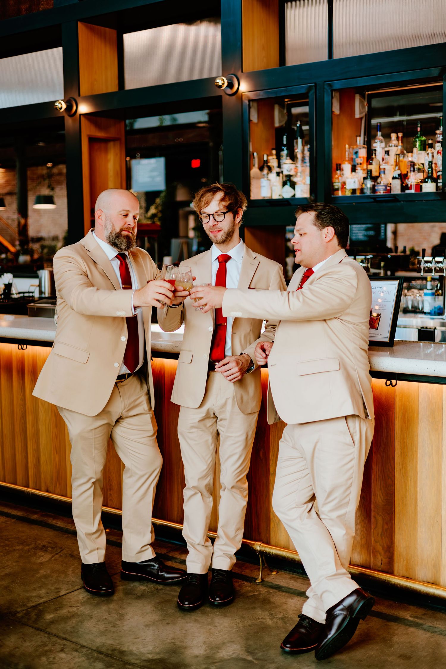 Three groomsmen in beige suits sharing a moment at the bar.