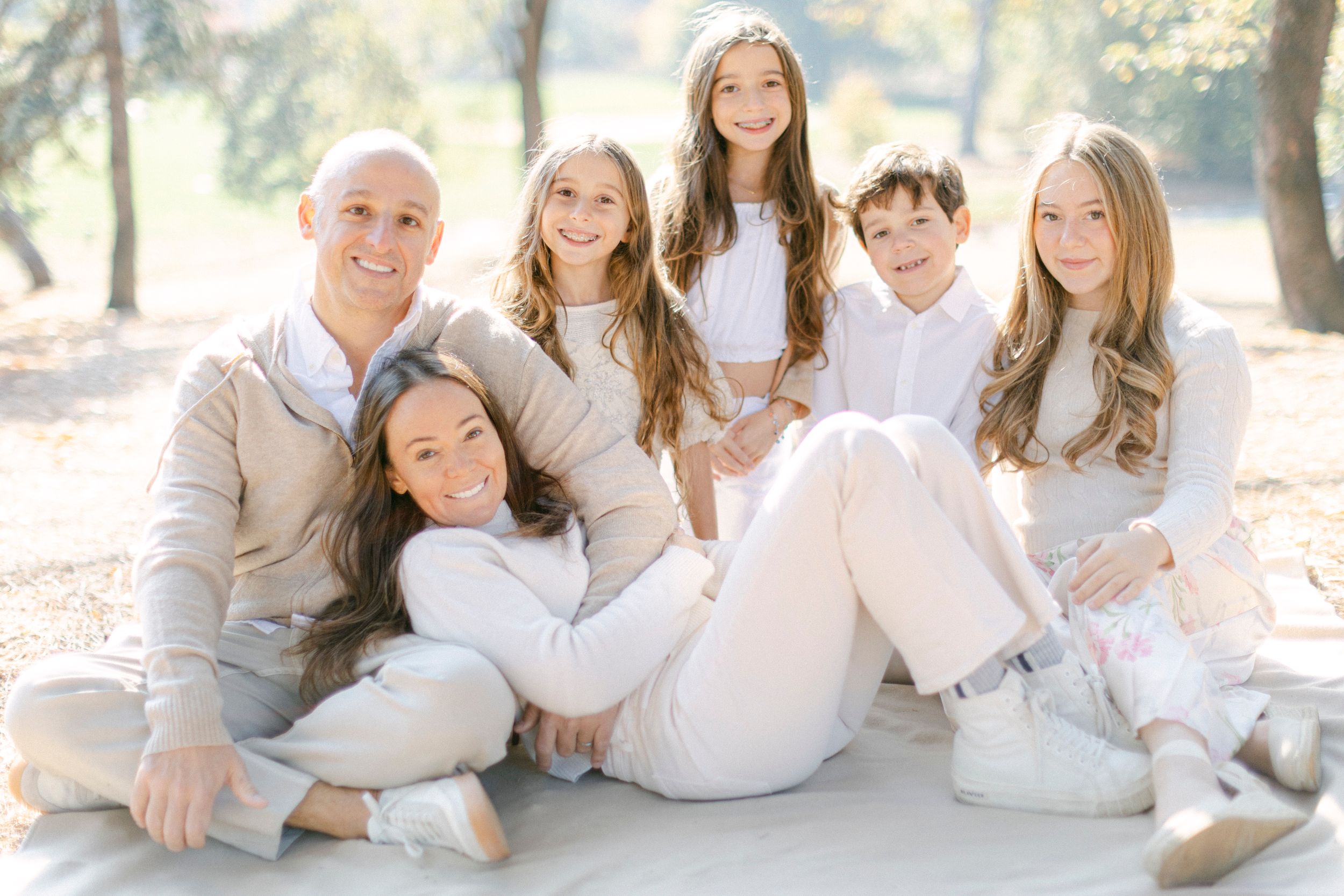 Family of six poses together outdoors wearing coordinated white and cream colored outfits.