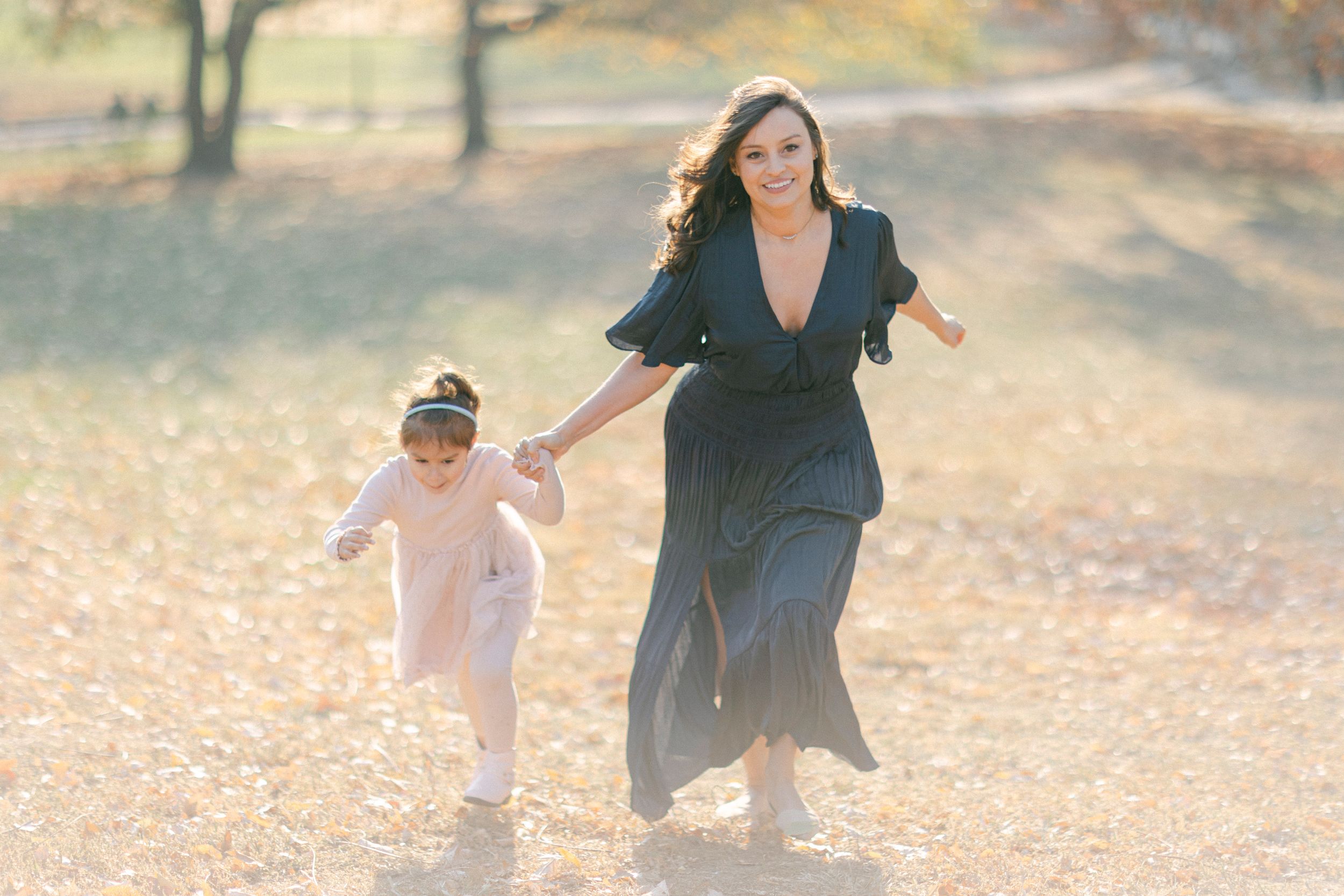 A joyful pair running together through an autumn field in flowing dresses.