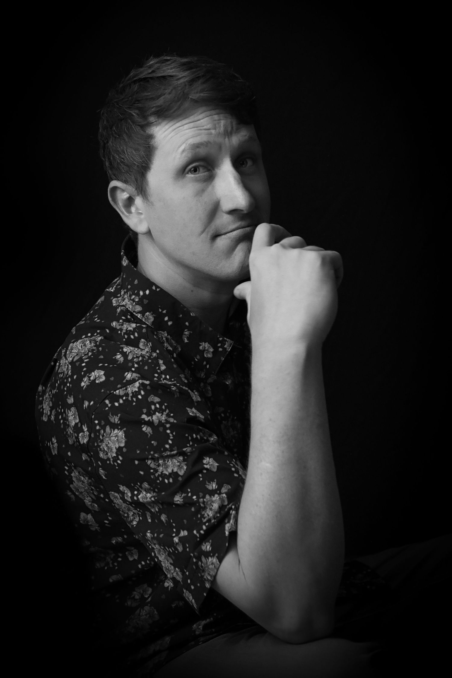 Black and white portrait photo of a person in a floral shirt with a thoughtful expression against dark background.
