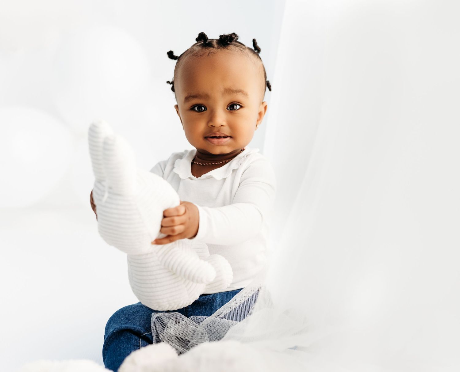Portrait of a toddler in white sweater and blue pants sitting against white background.