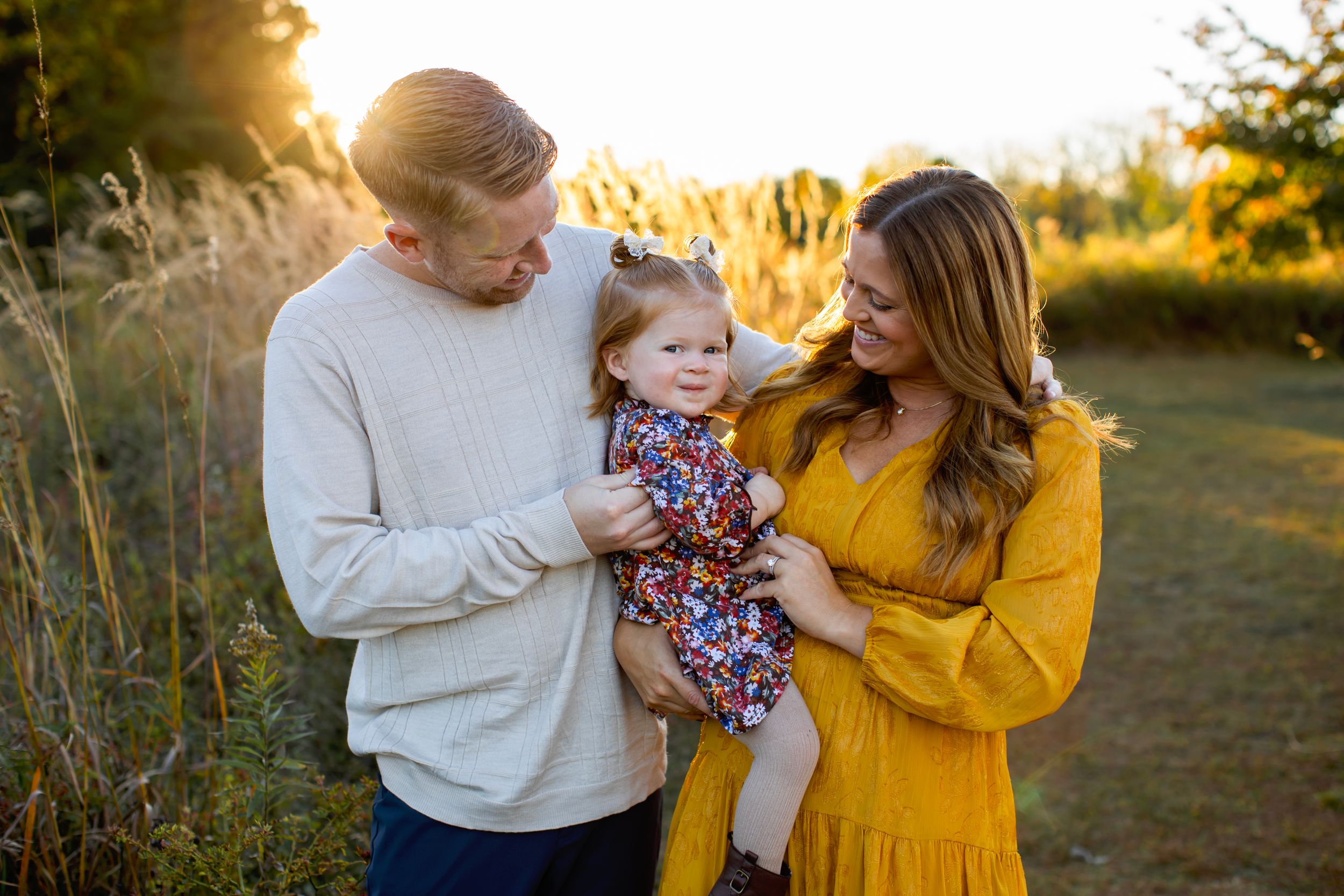 A family shares a tender moment together in a sunlit field during golden hour in Sussex County NJ with Sarah Jane Photography LLC