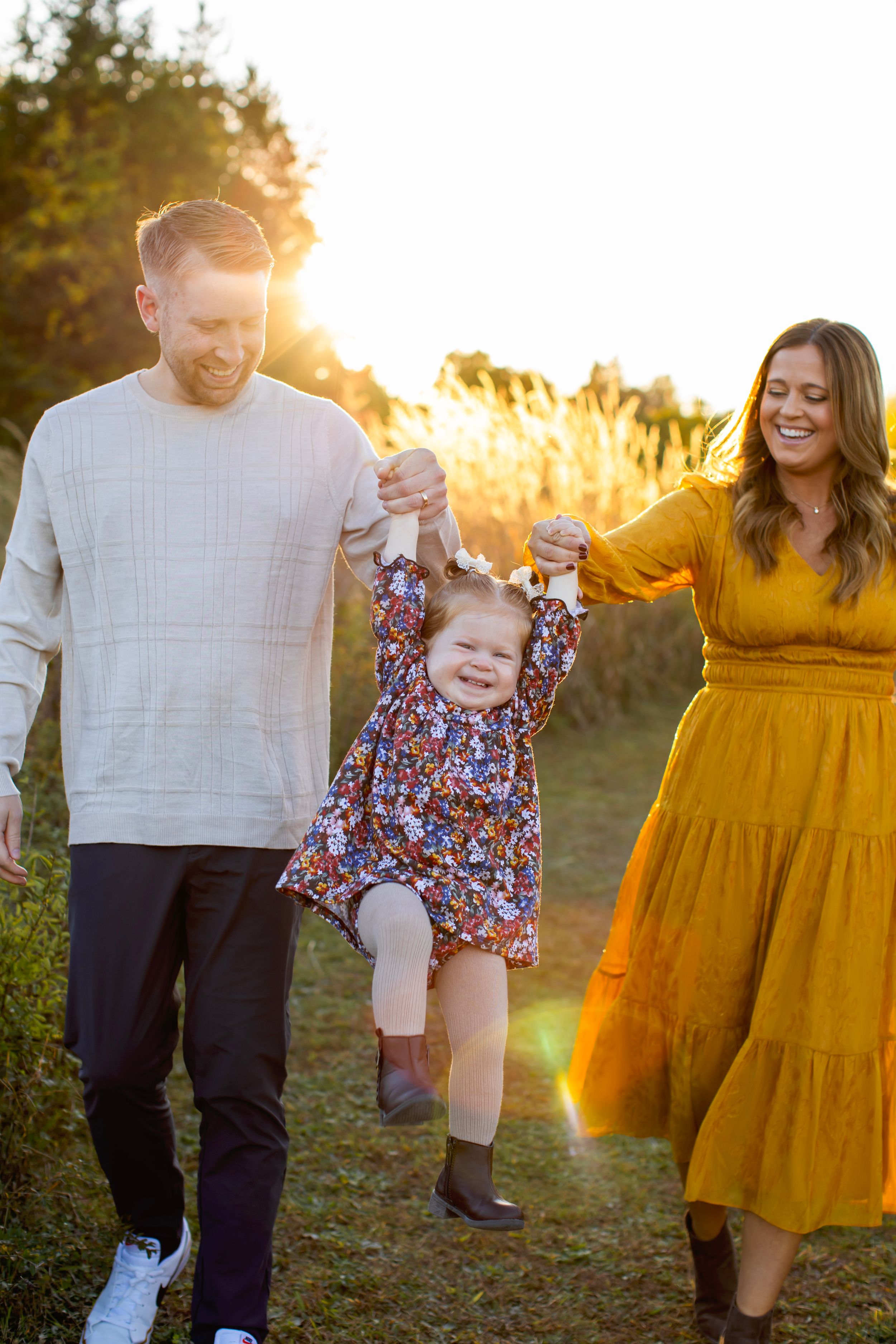 Family enjoys a playful moment swinging child between them during golden sunset in Sussex County NJ with Sarah Jane Photography LLC