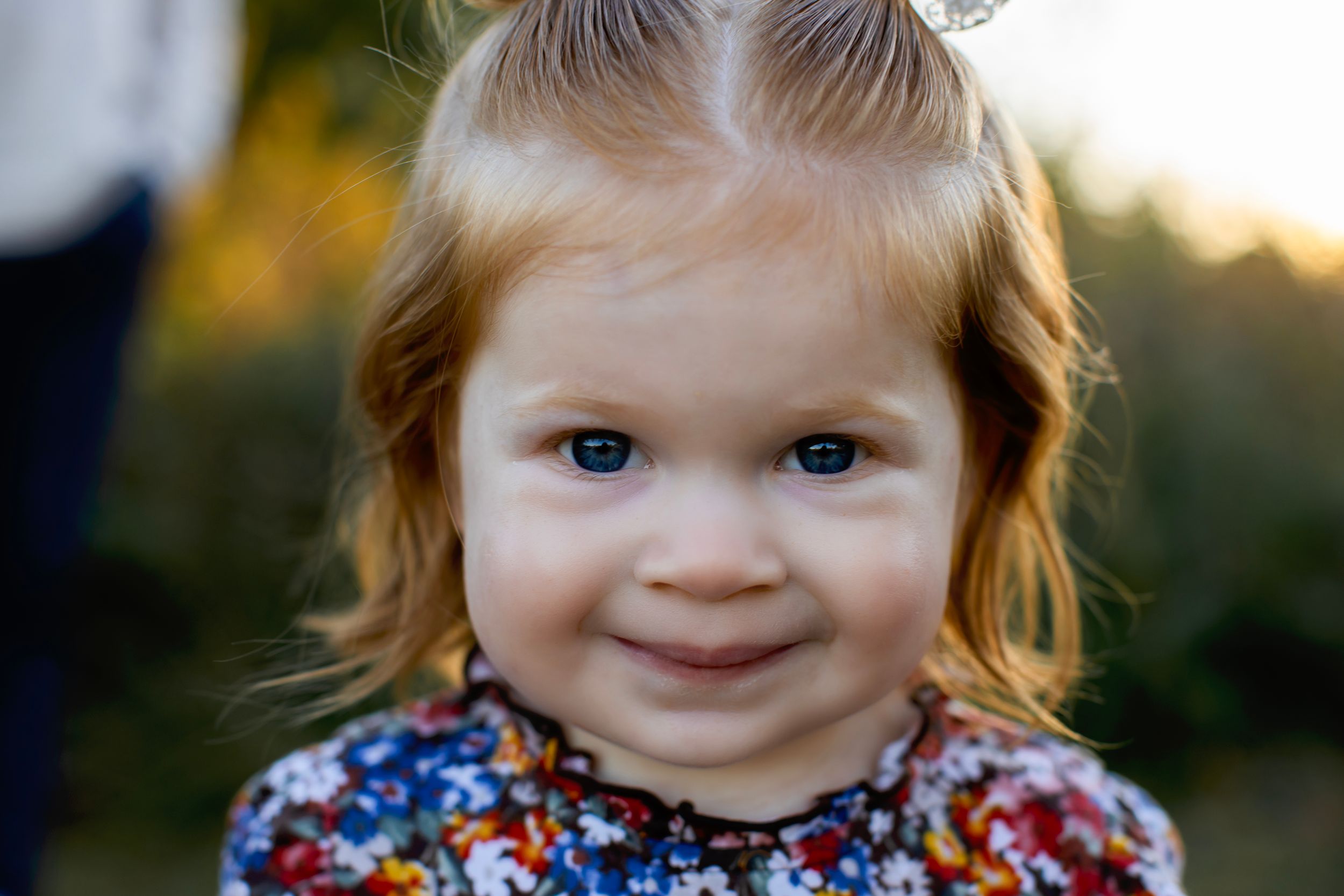 Close up outdoor portrait of a toddler wearing a floral dress in soft golden sunlight. NJ Family Photographer