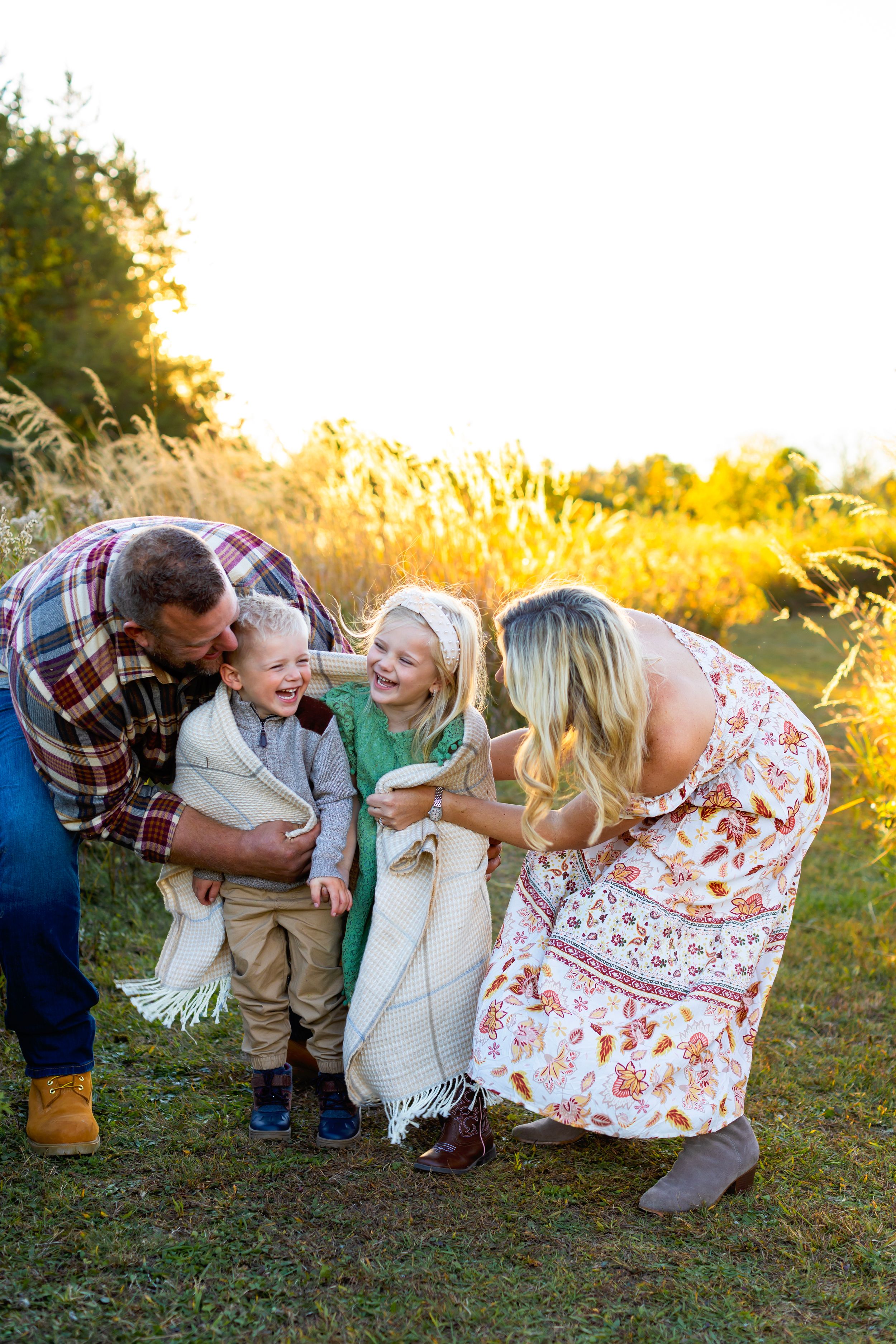 A family shares a joyful moment together outdoors during golden hour in a grassy field. NJ Family Photographer