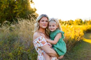 Two people in a floral dress and green dress embrace in a sunlit field with tall grass at golden hour. NJ Family Photographer