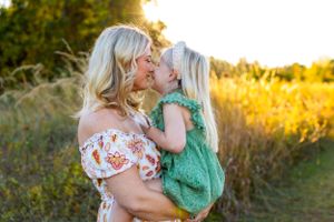 A tender moment shared between two people in a sunlit field at golden hour wearing floral and green lace dresses. NJ Family Photographer
