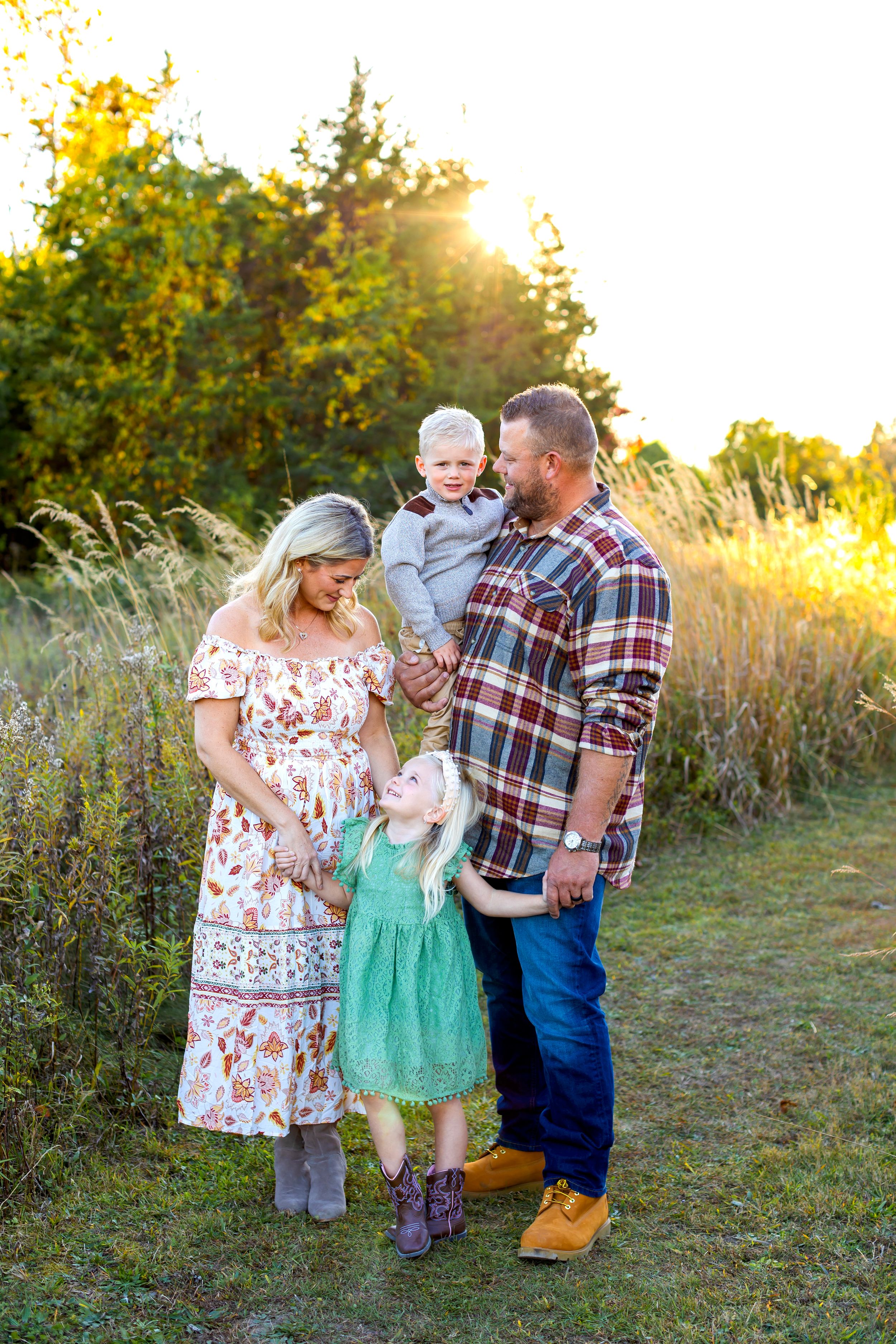 A family poses together at golden hour in a meadow with evergreen trees and warm sunlight in the background. NJ Family Photographer
