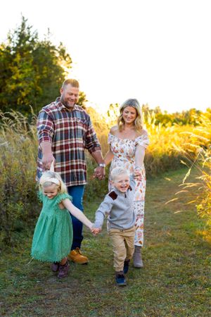 A family enjoys a sunset stroll together on a nature path as golden light filters through trees behind them. NJ Family Photographer